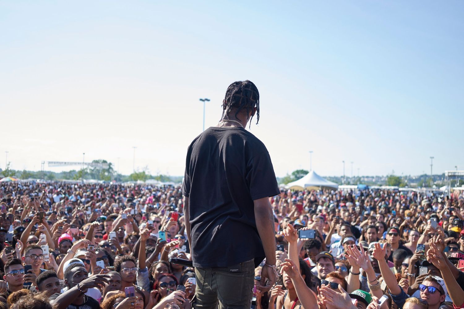 Large festival crowd raises hands in unison during an outdoor daytime concert performance under blue skies.