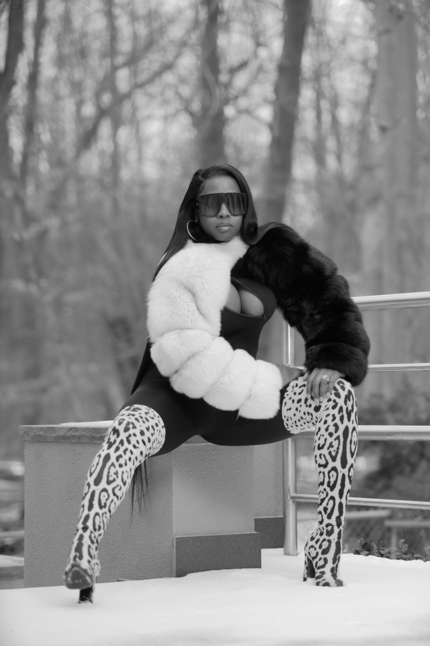 A winter fashion shot featuring leopard print boots and a black and white fur coat in a snowy forest setting.