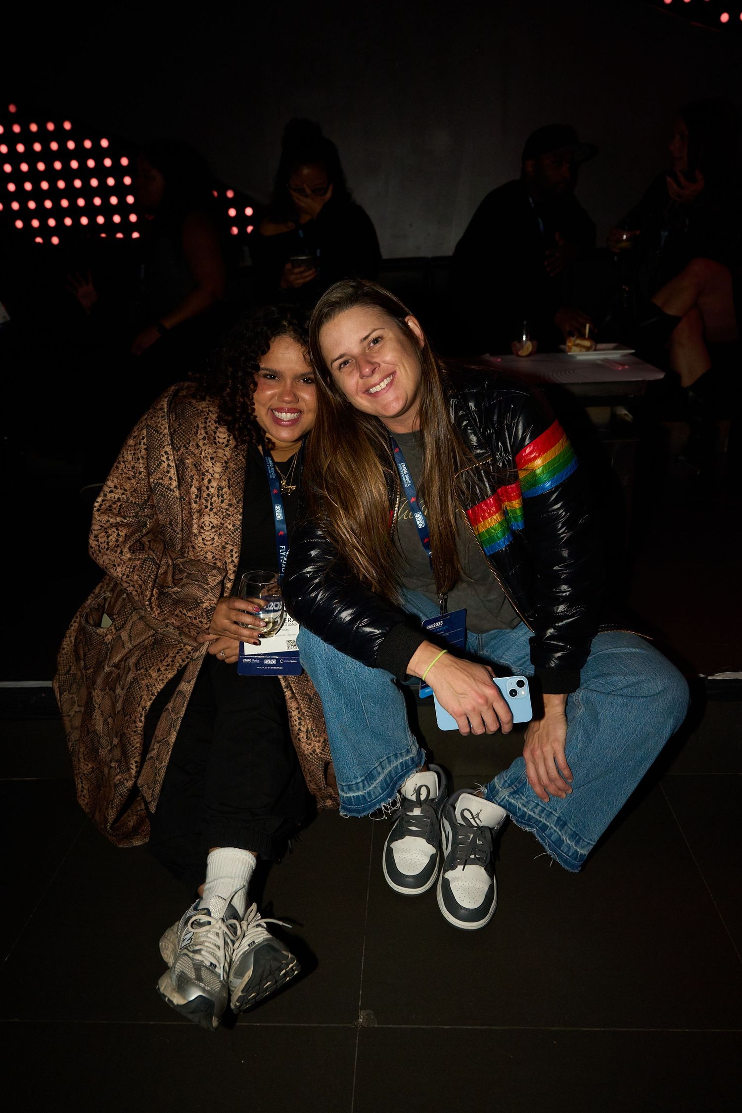Friends sitting together on floor at event wearing casual attire including denim and sneakers.