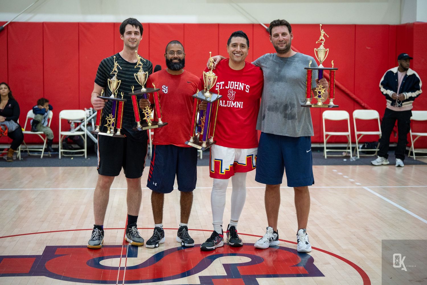 A group of people standing together in a gym with red walls and sports equipment visible in the background.
