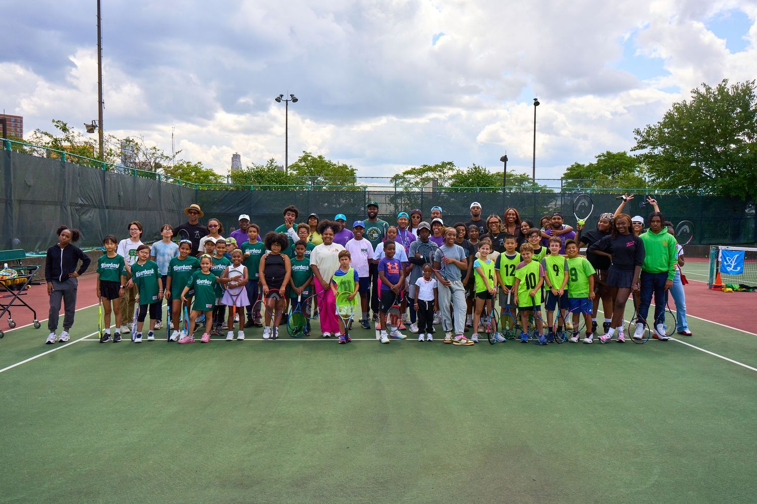 Large group of tennis players and coaches gathered on outdoor courts for a group photo session.
