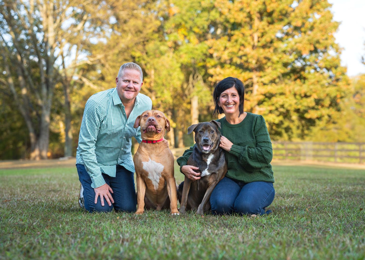 A dog photoshoot of Two rescue mixed-breed dogs sitting with their owners in a tree-filled park in Warner Robins, Georgia.