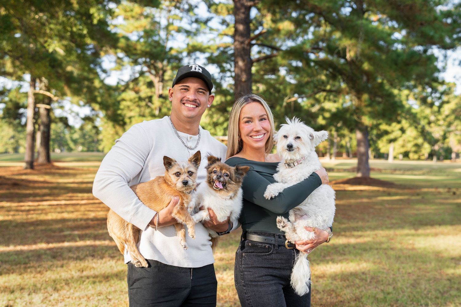 Family photo of two people holding three brown and white dogs at the park.