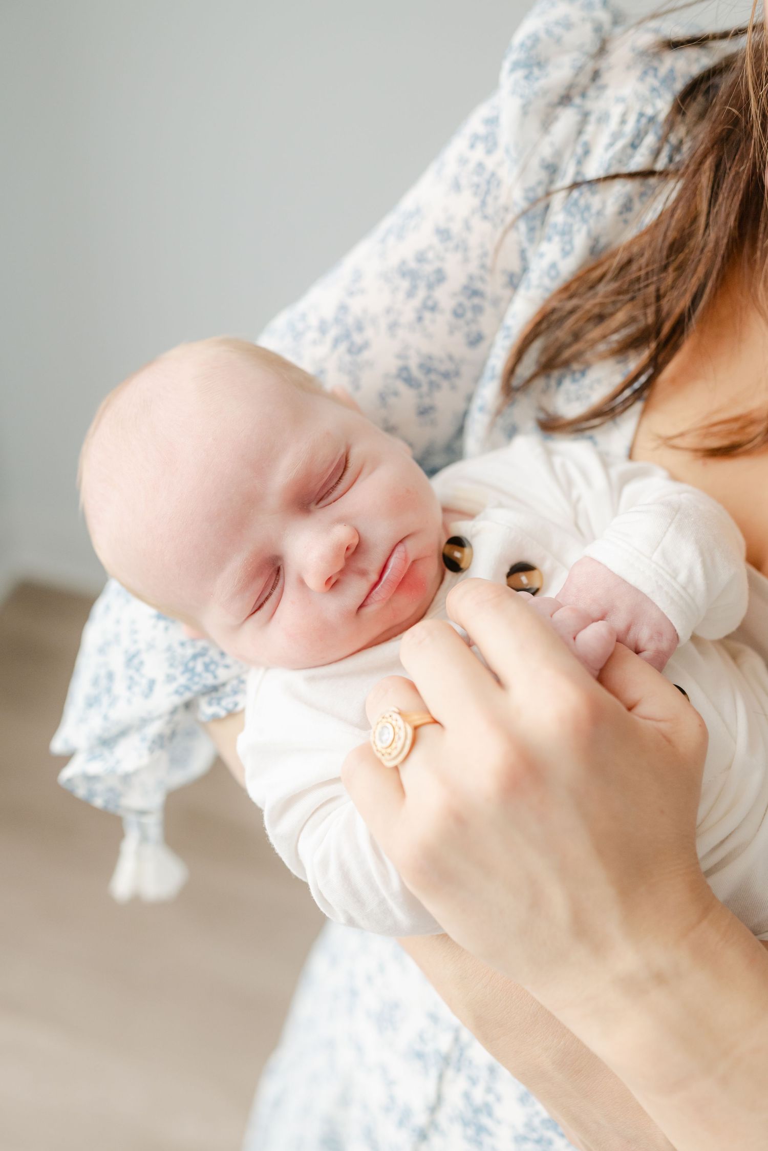 Sleeping newborn baby with peaceful expression being held in floral dress.