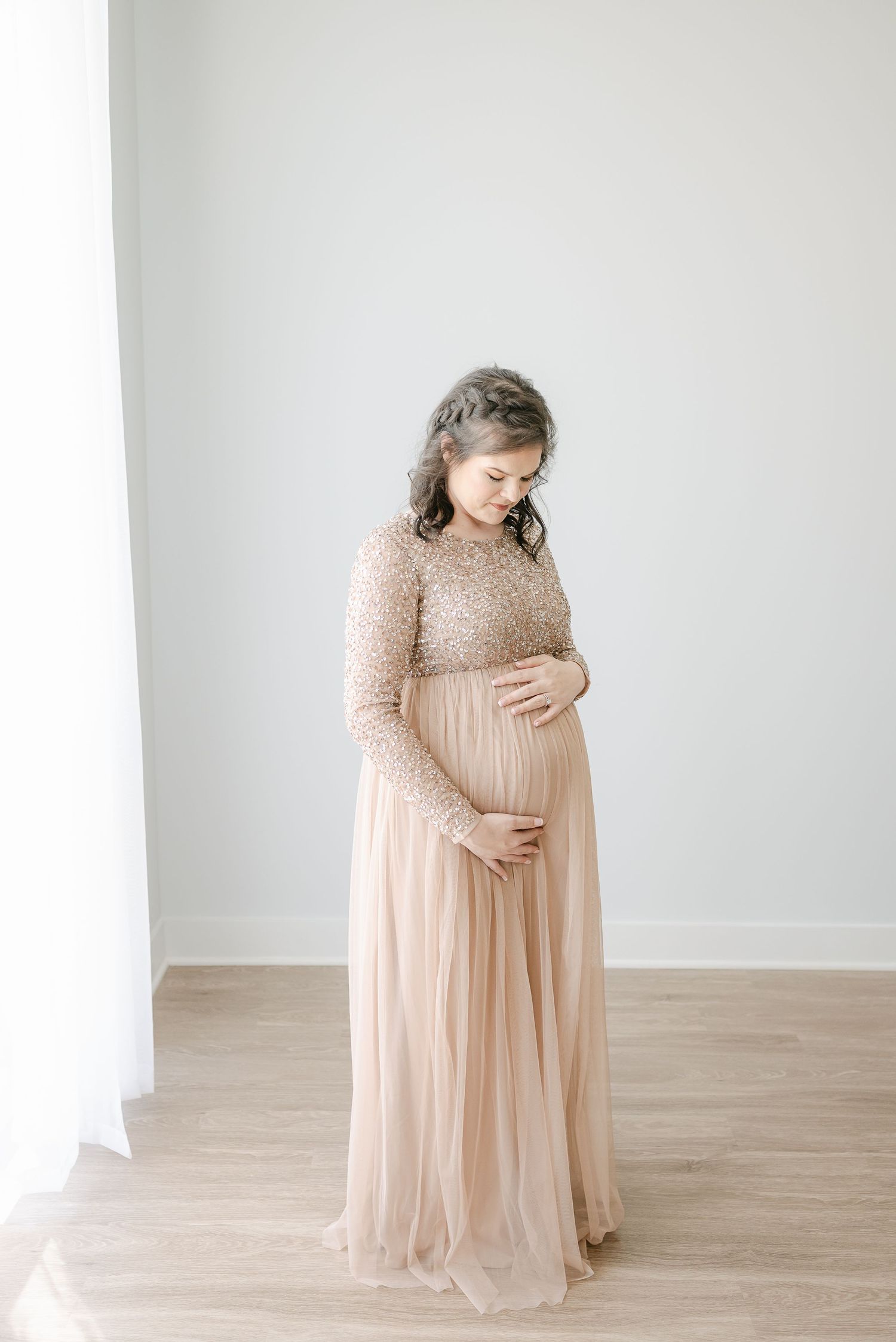 Woman in a flowing beige dress with sequined bodice stands in an elegant indoor setting.