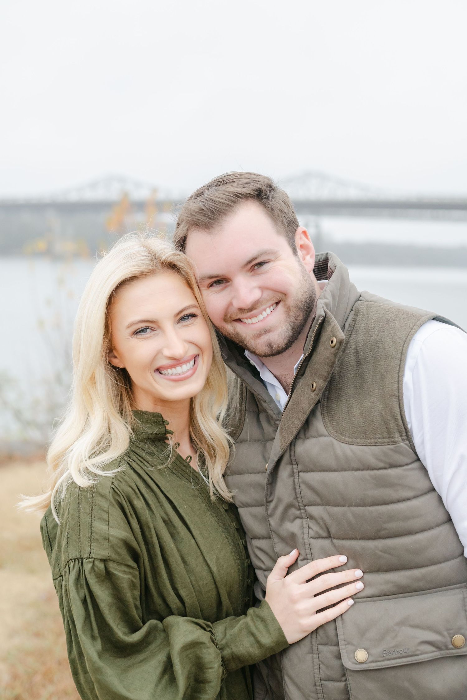 A couple in casual fall attire smiling and embracing outdoors during an engagement photo session.