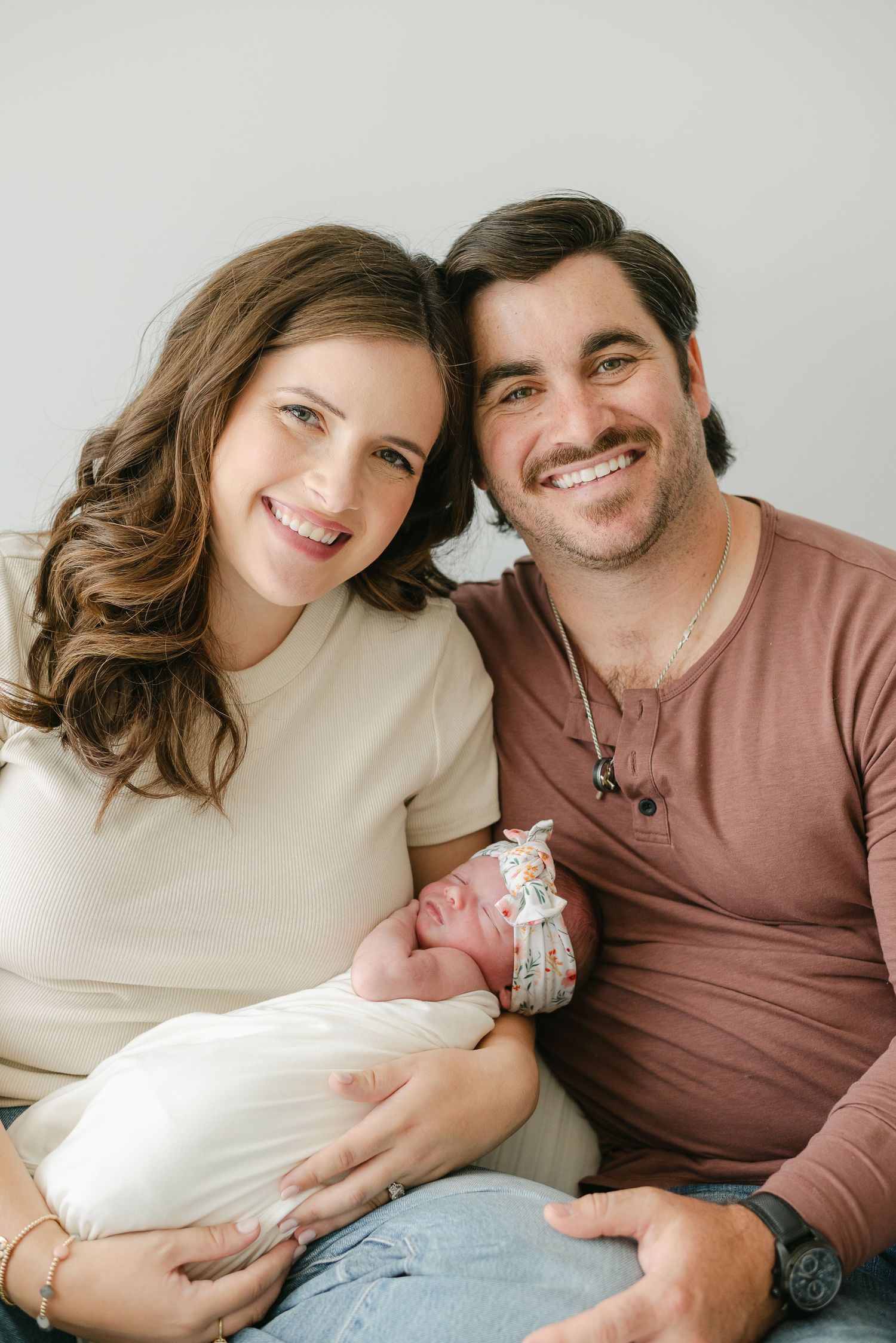 Parents share a tender moment with their newborn baby against a light gray background.