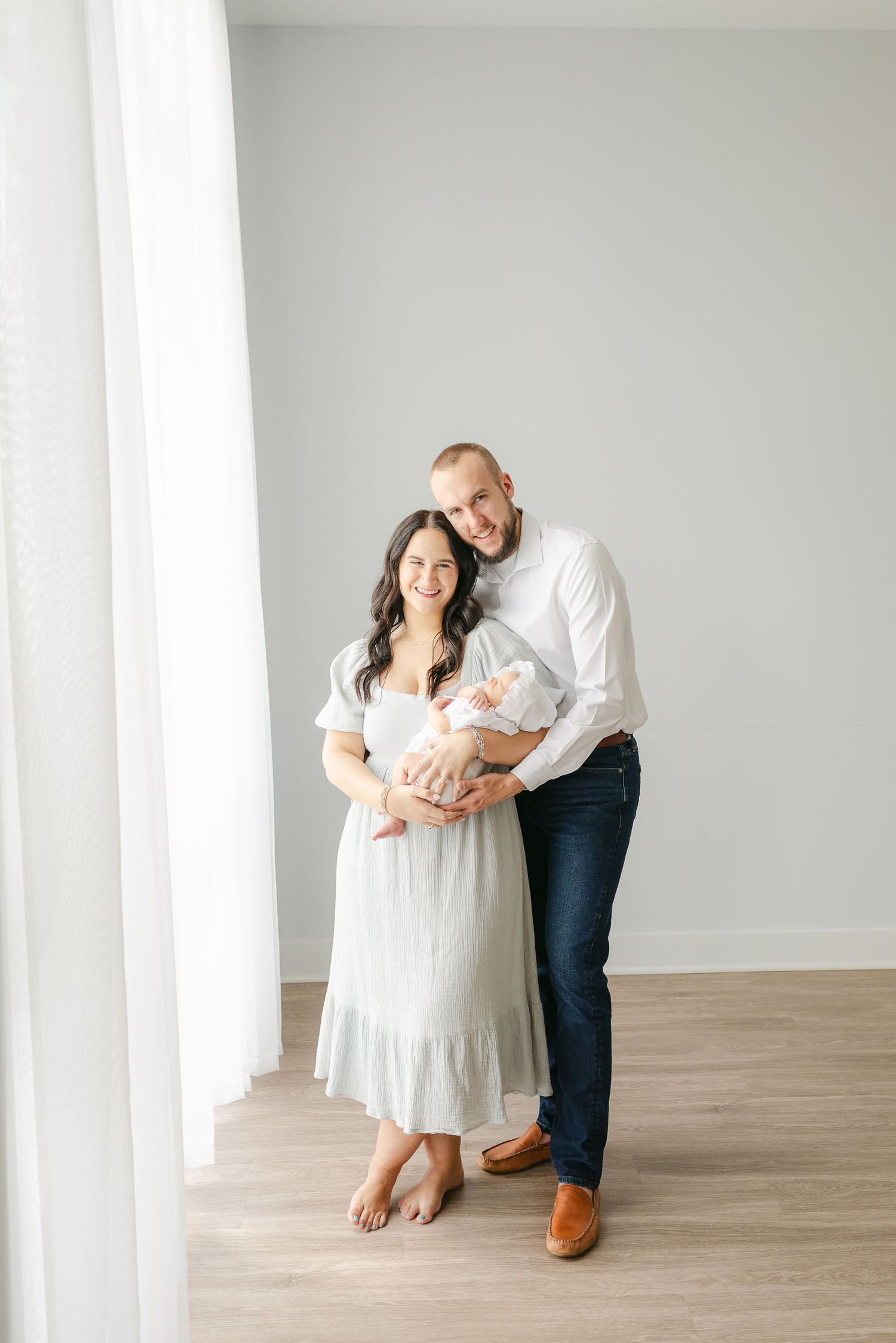 Family portrait session in a minimalist room with white walls and wooden floors.