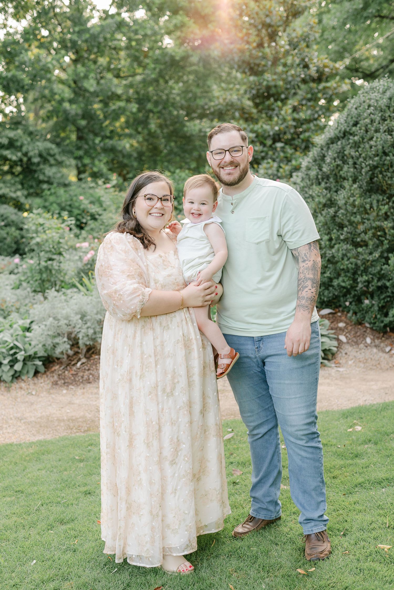 A family poses together on a garden path during a sunny outdoor portrait session.