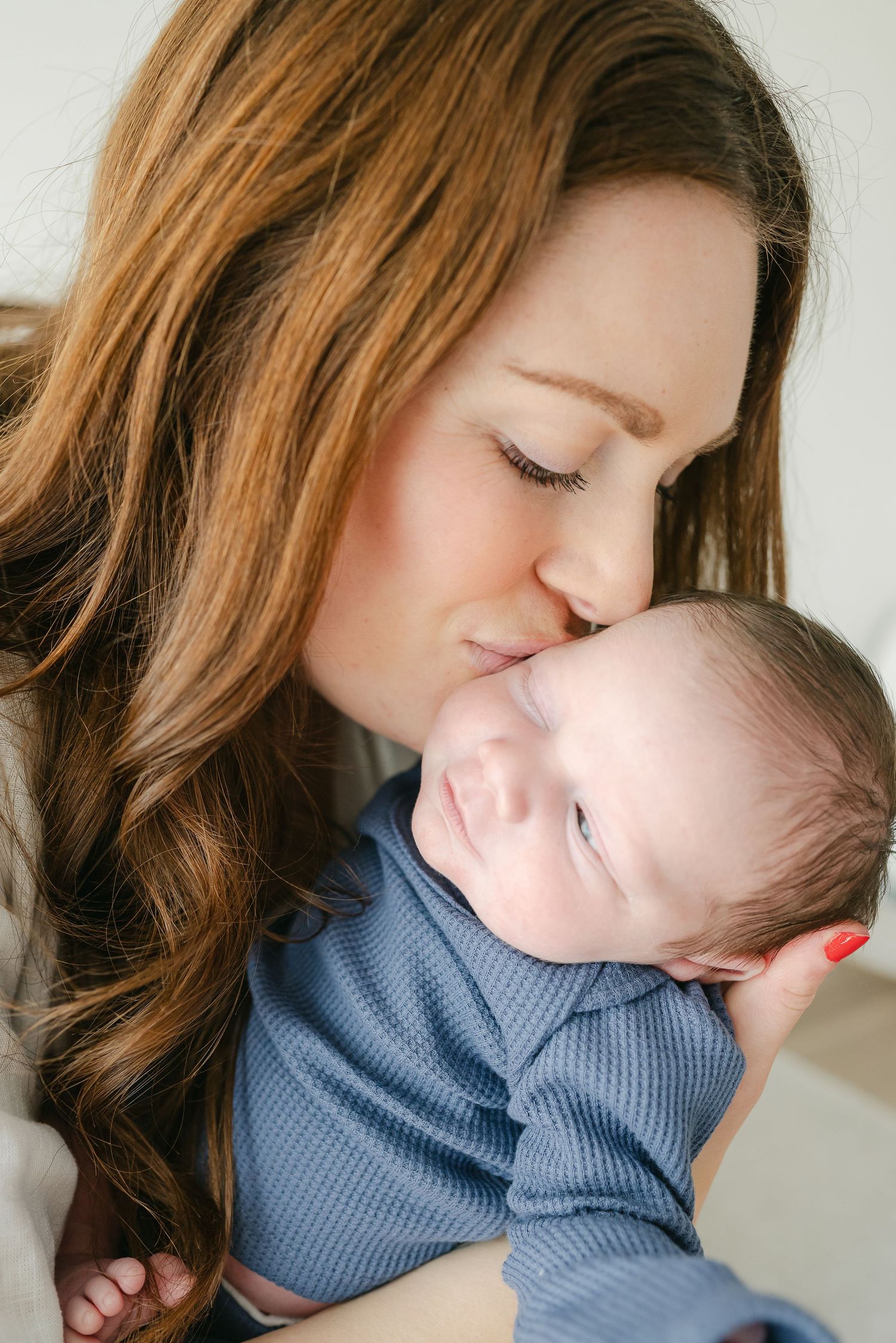 Mother cradling baby wearing blue knit sweater in intimate portrait series.