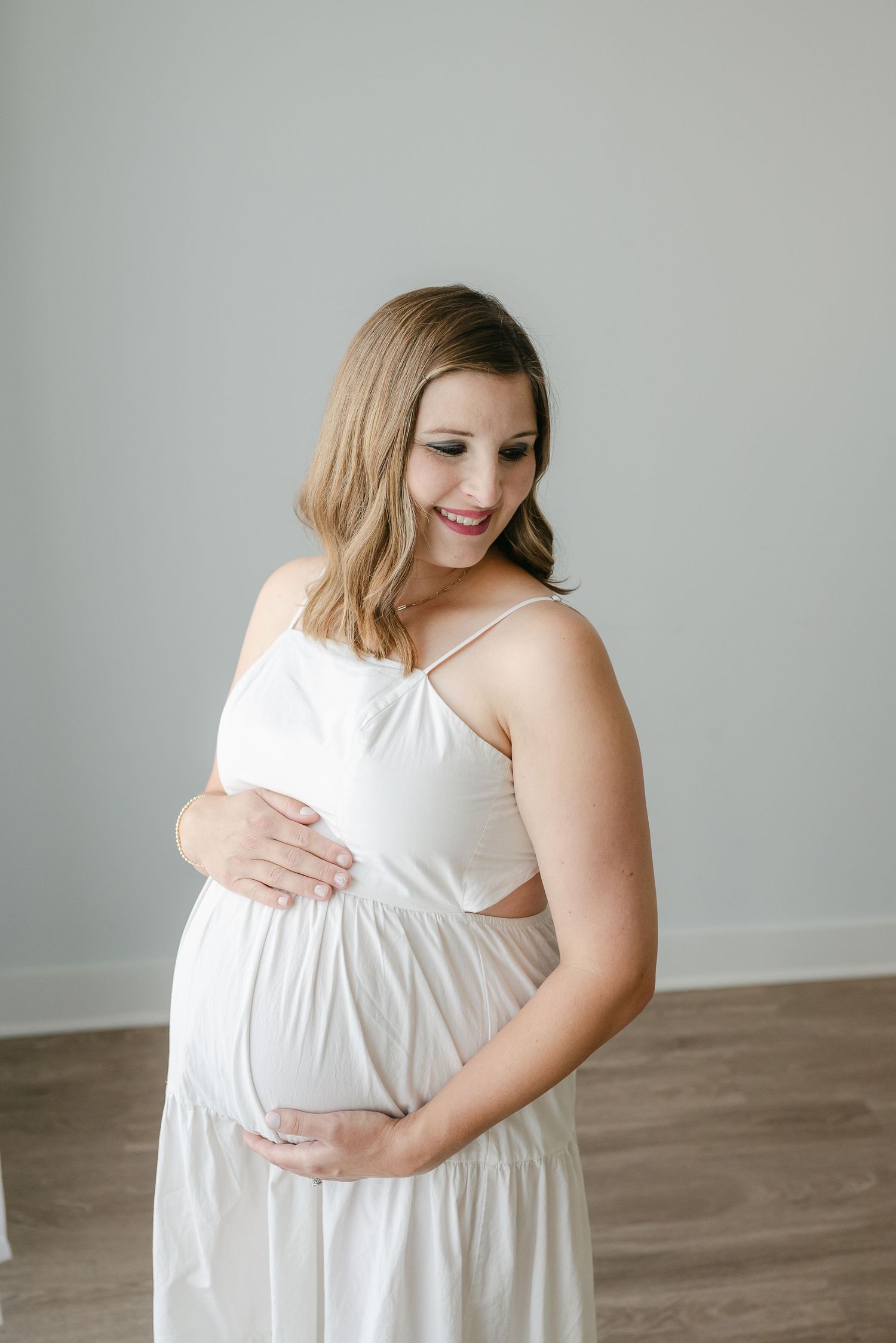 A person in a flowing white dress poses for indoor maternity photos.