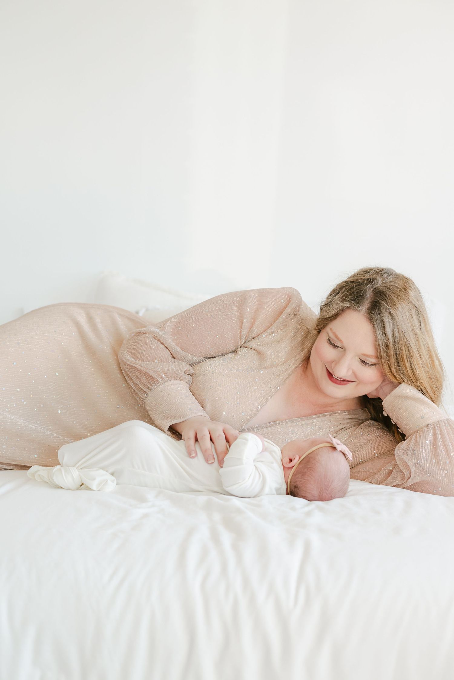 Mother and newborn sharing tender moment on white bedding.