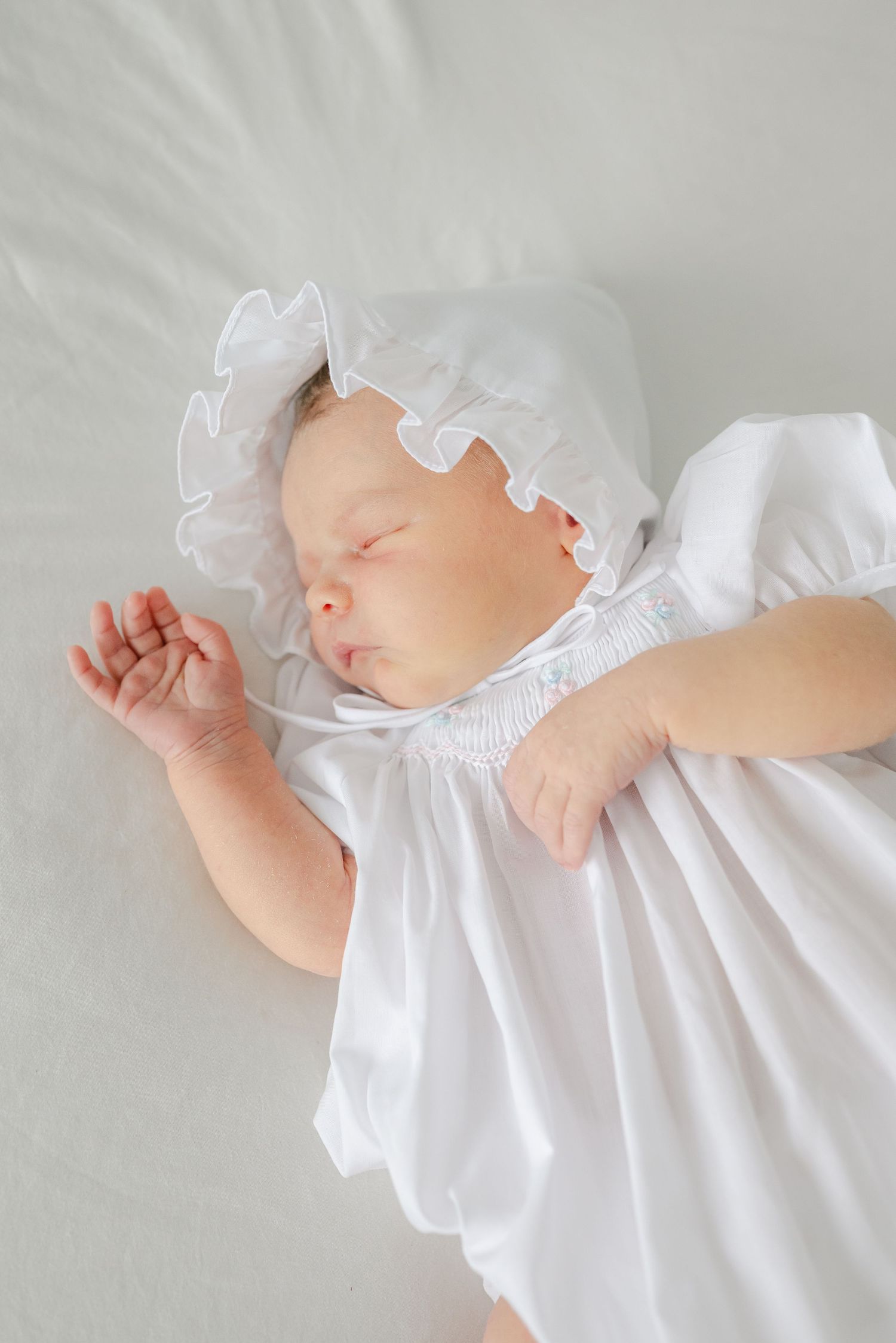 Delicate details of a baby wearing a white ruffled dress against a light background.
