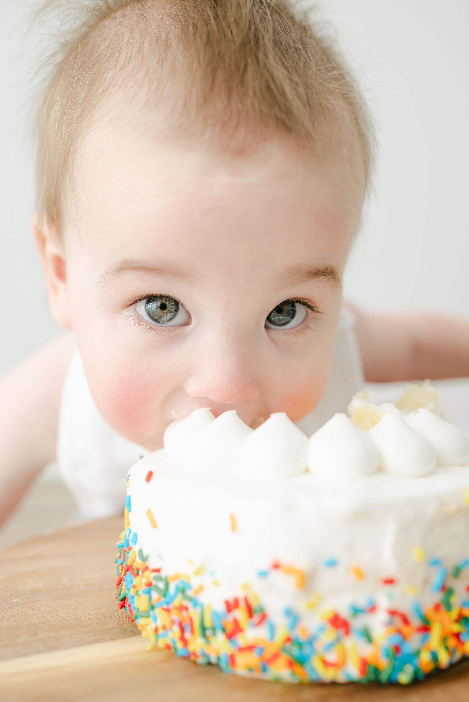 Close up of a baby with bright eyes enjoying a colorful birthday cake with sprinkles.