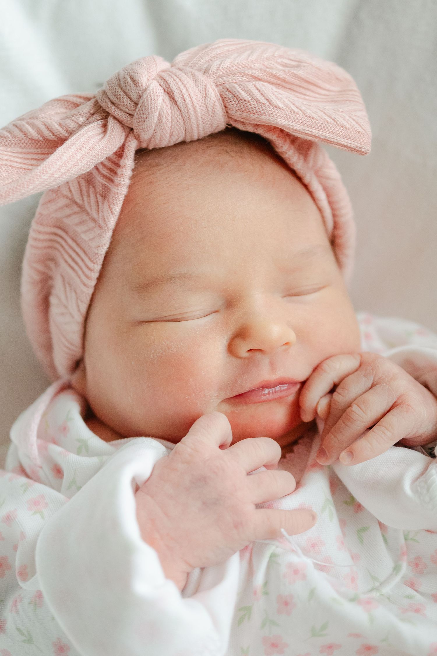 Sleeping newborn wearing pink headband and floral outfit in soft natural light.