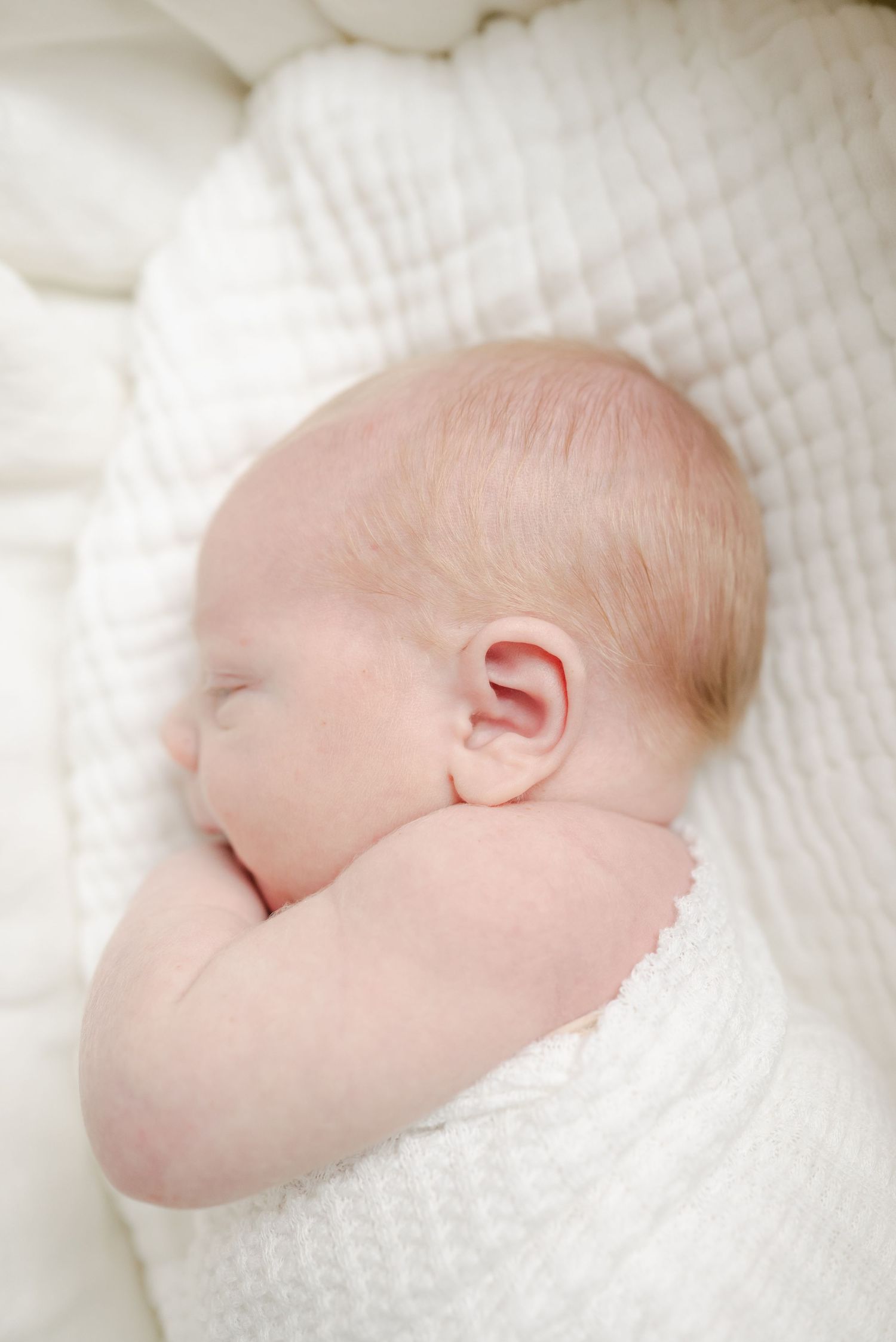 Peaceful sleeping newborn wrapped in white blanket against textured bedding.