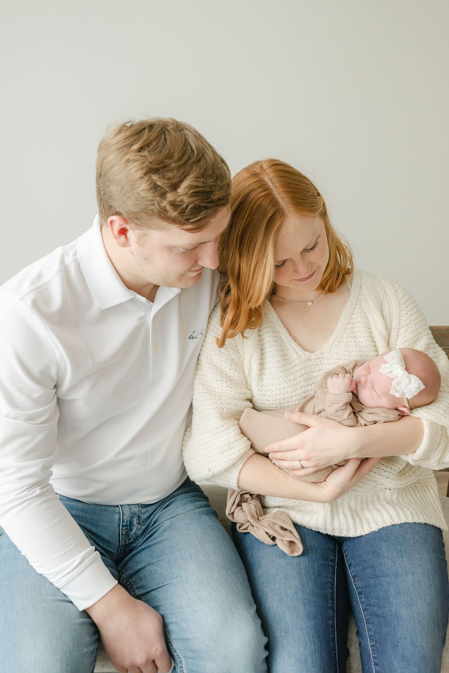 Parents sitting together on floor bonding with their newborn baby in intimate family portraits.