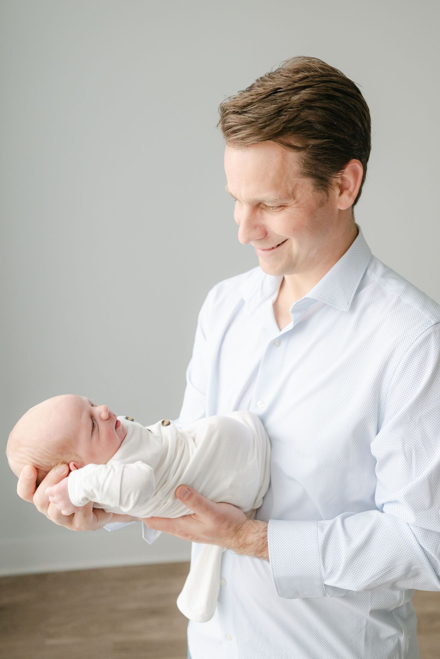 Person in white button-down shirt tenderly holds sleeping newborn baby.