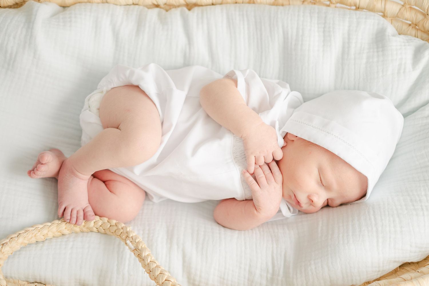 Peaceful sleeping newborn in white outfit lying on soft white bedding.
