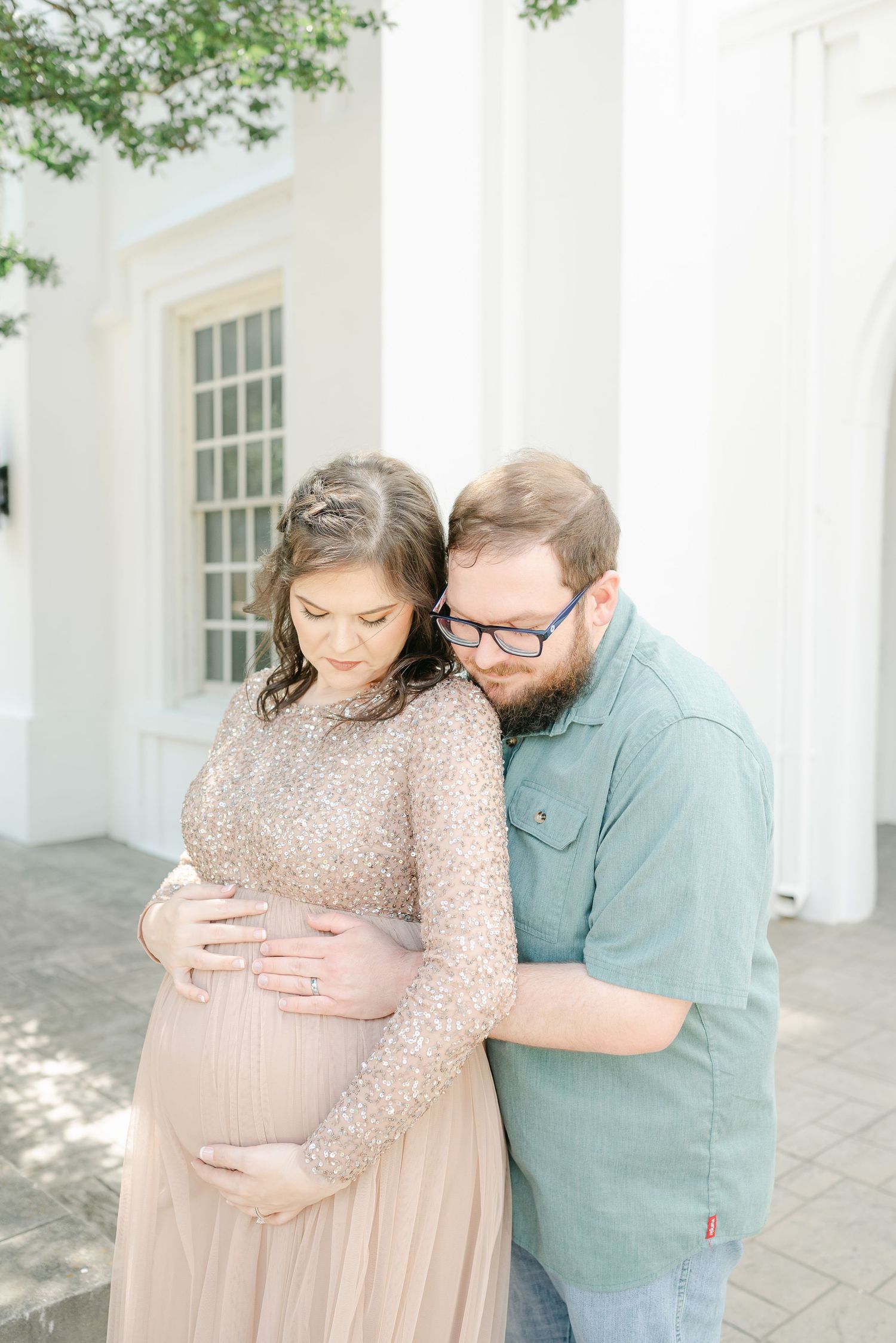 Couple shares intimate moment during maternity photoshoot on a white columned porch.