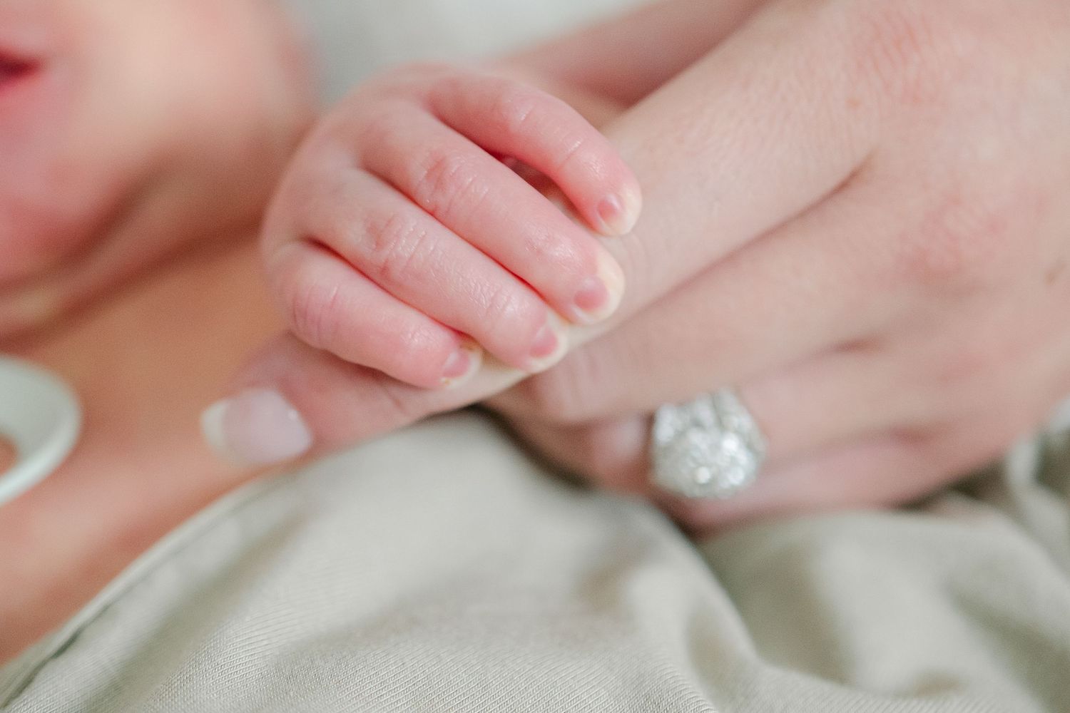 Close-up of hands with an engagement ring resting on soft fabric.