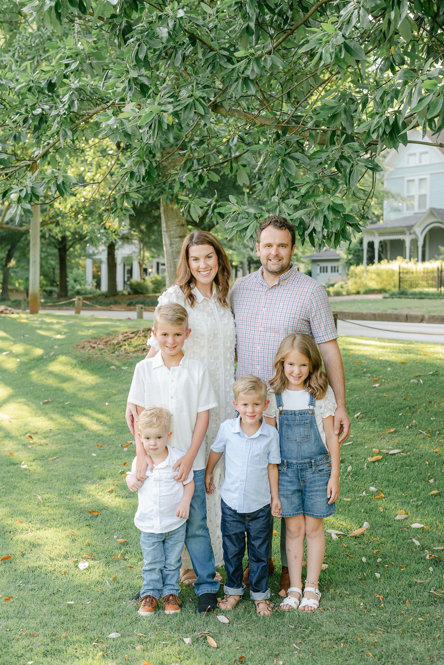 Family of five posing together on a sunny lawn with historic house in background.
