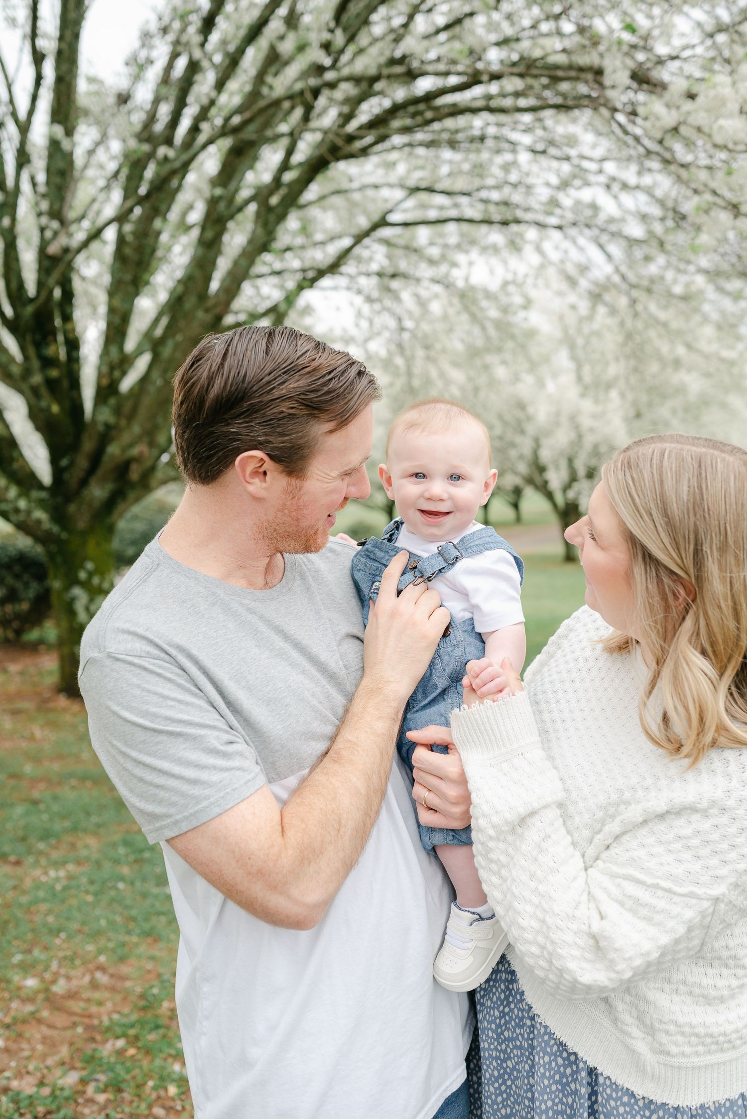 A happy family shares joyful moments together under blooming trees in a spring orchard setting.