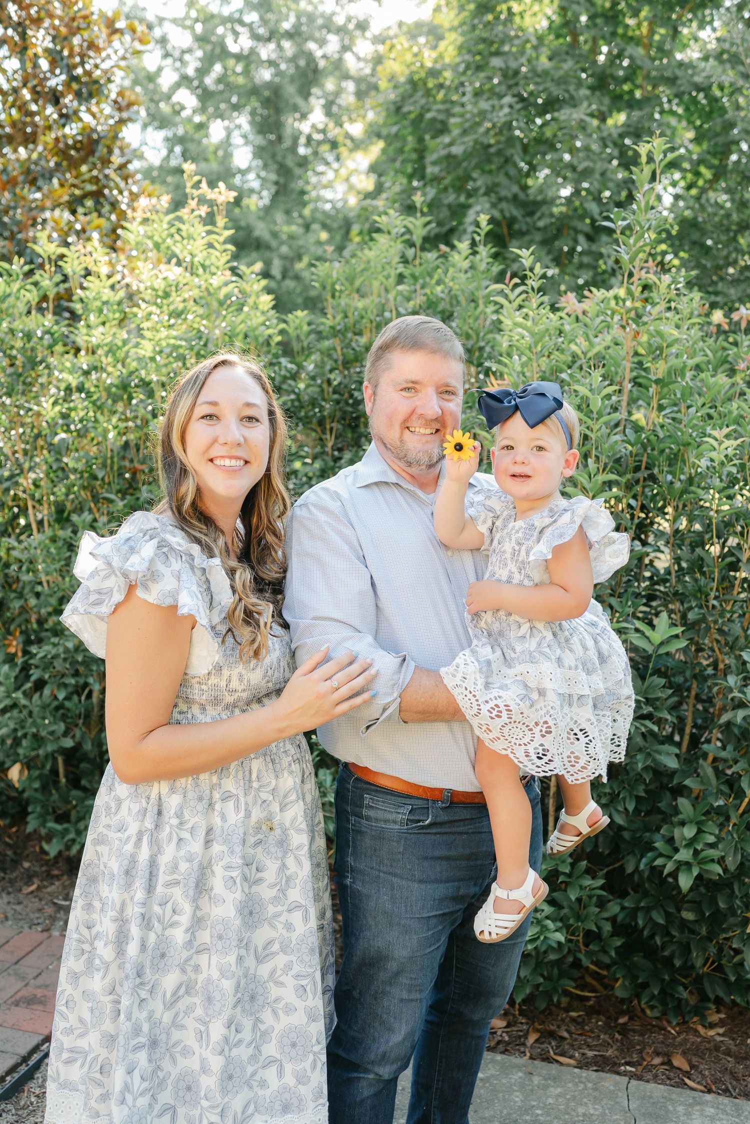 Family shares joyful interaction in lush garden setting wearing coordinated outfits.