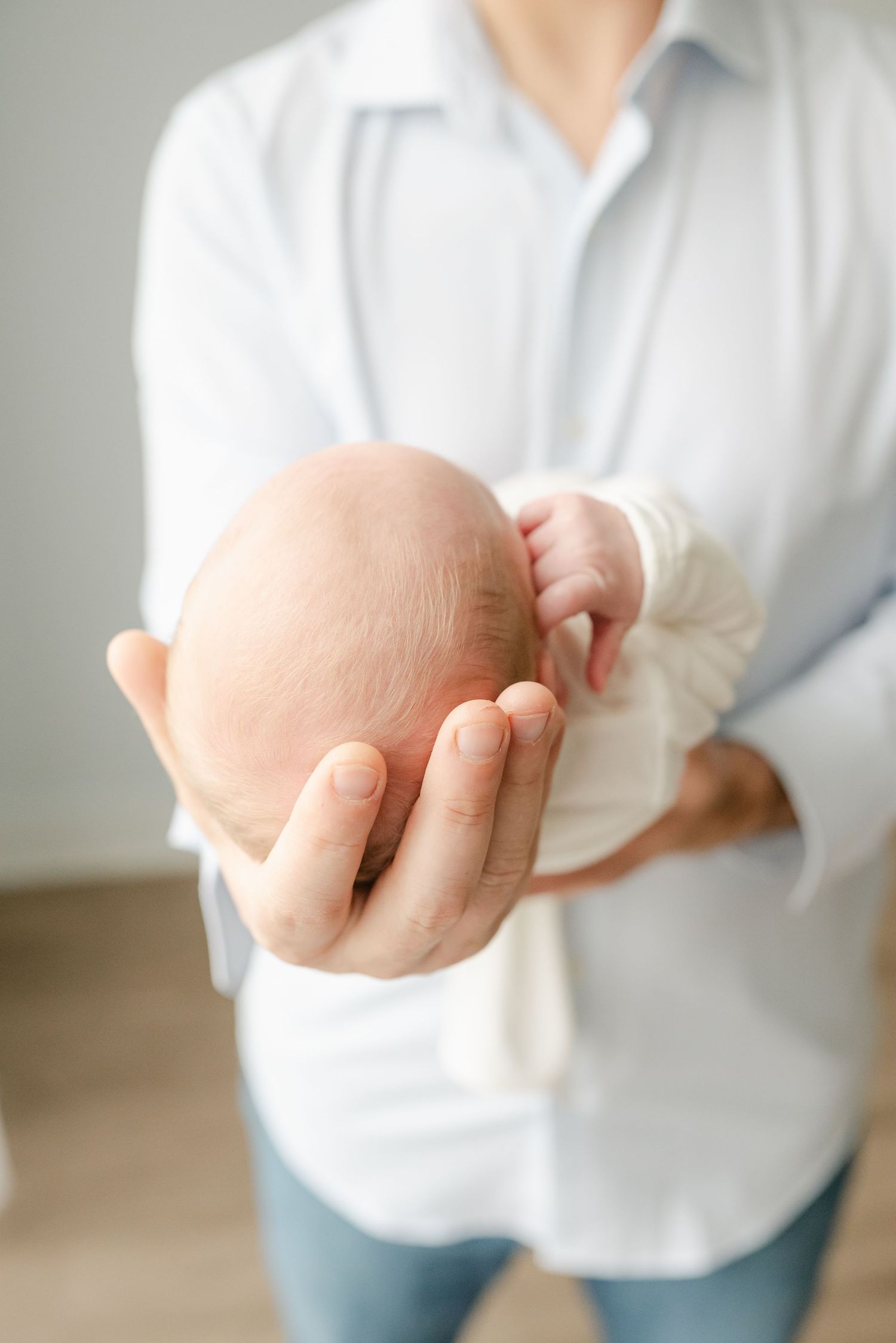 Close-up of hands cradling a sleeping newborn baby in white clothing.