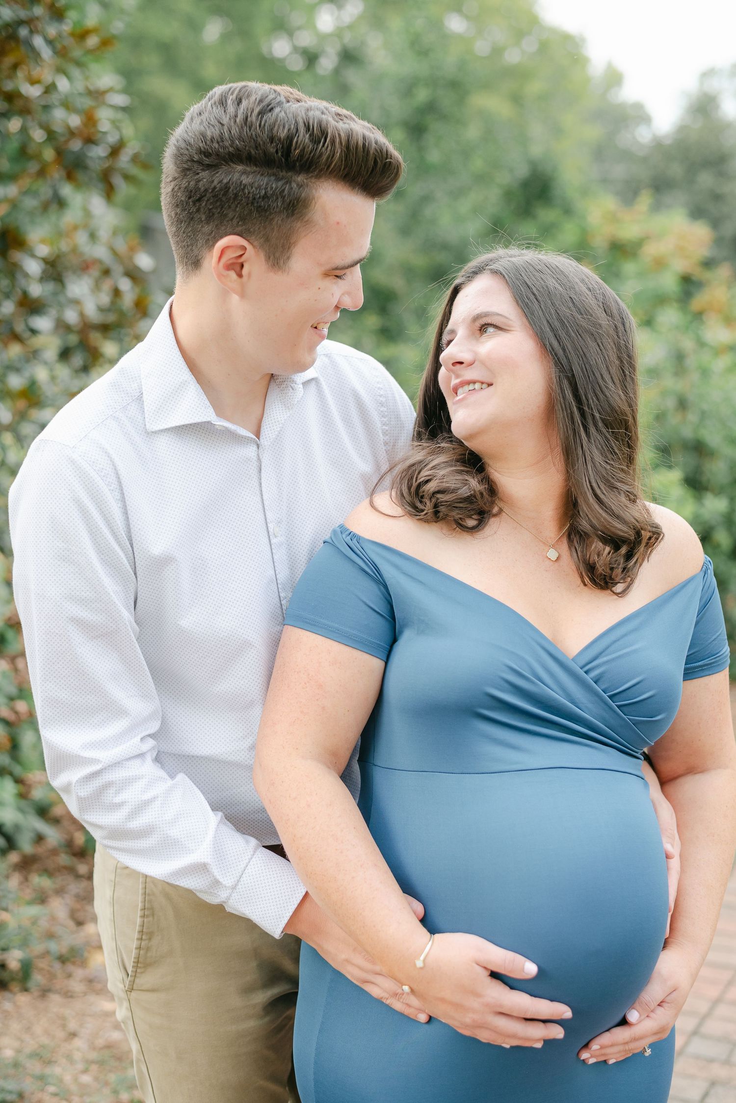 A couple shares tender moments while expecting in an outdoor garden setting.