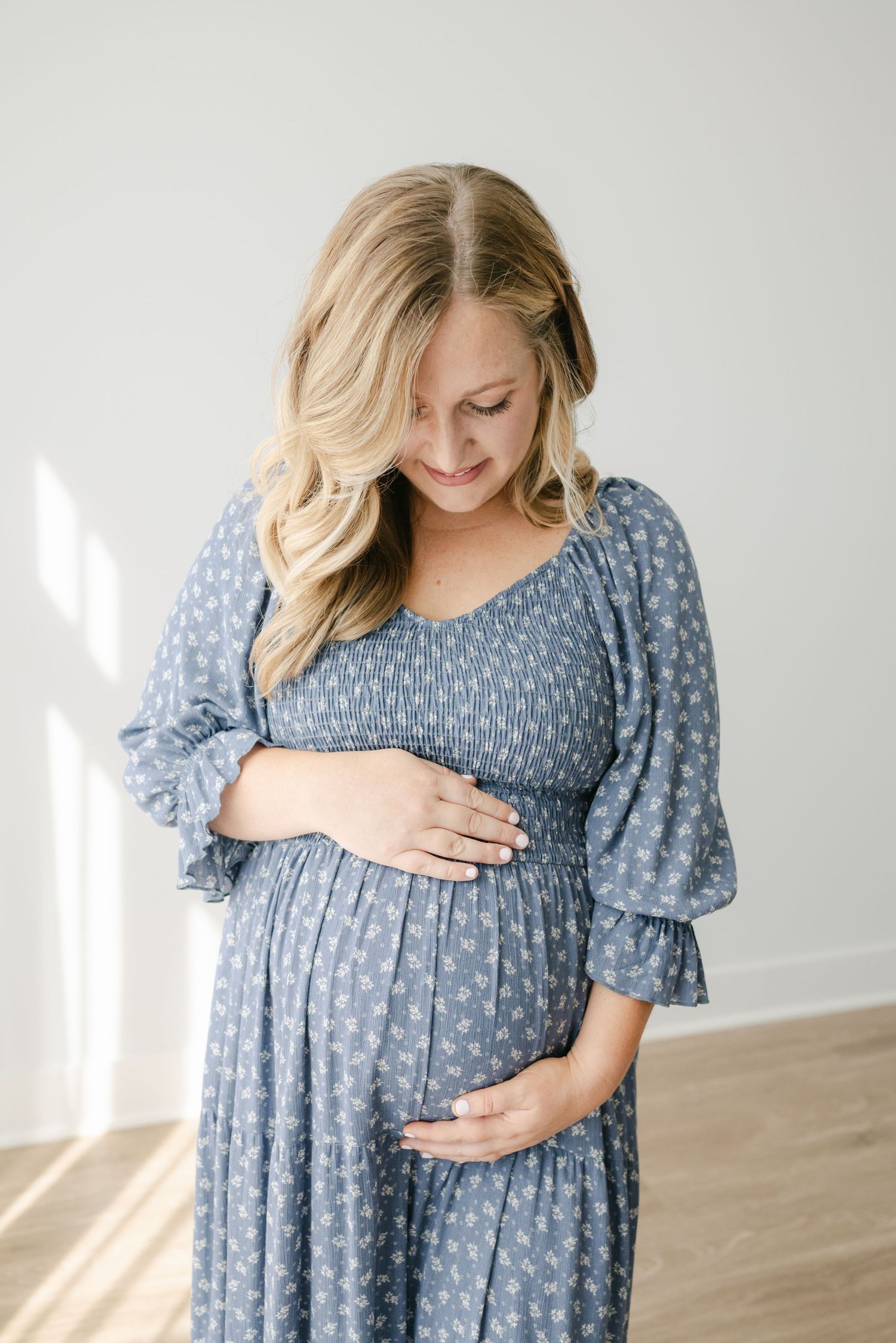 Maternity portraits in a blue patterned dress against white studio backdrop.