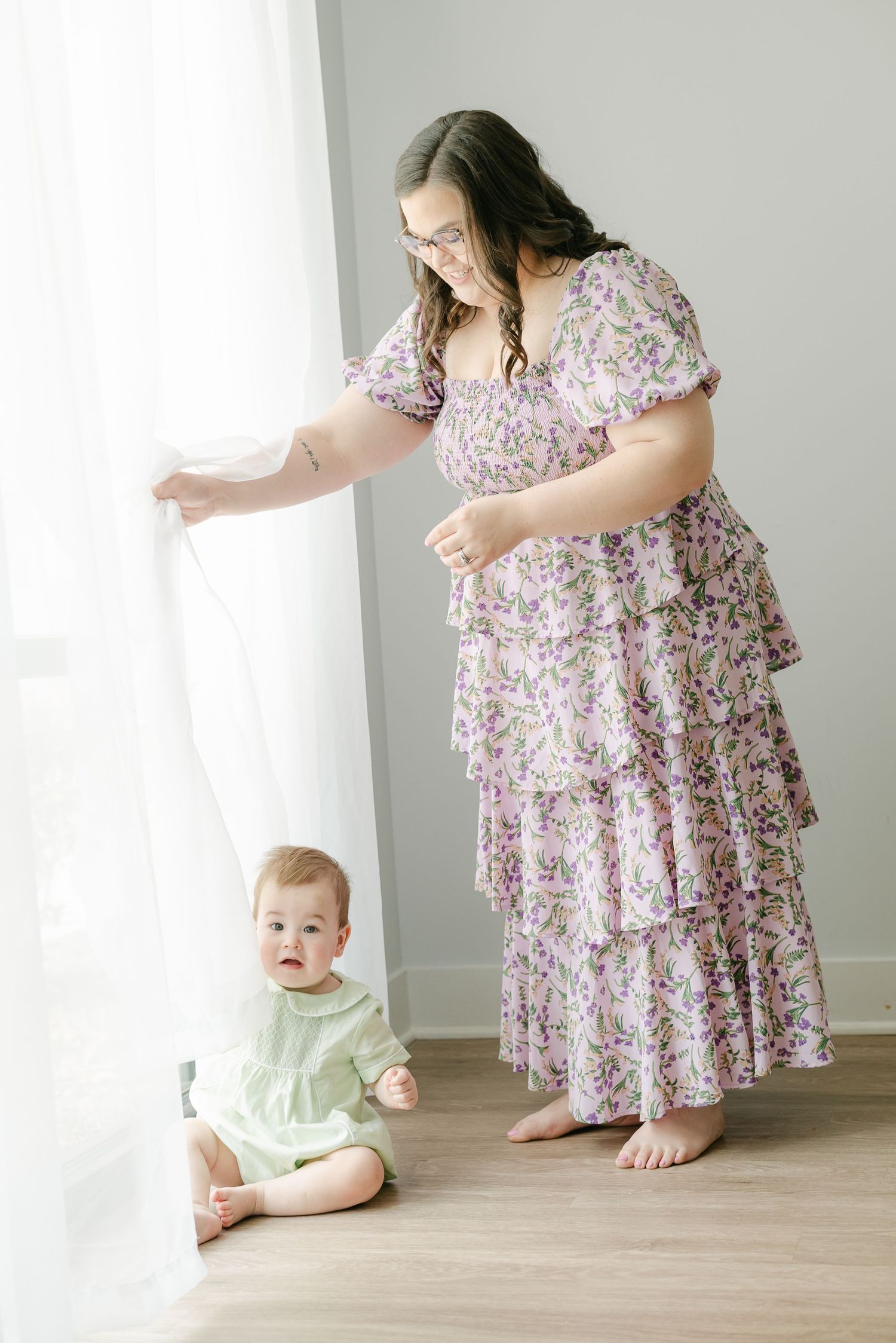 Sweet candid moments between parent and baby on hardwood floor with flowing purple floral dress.