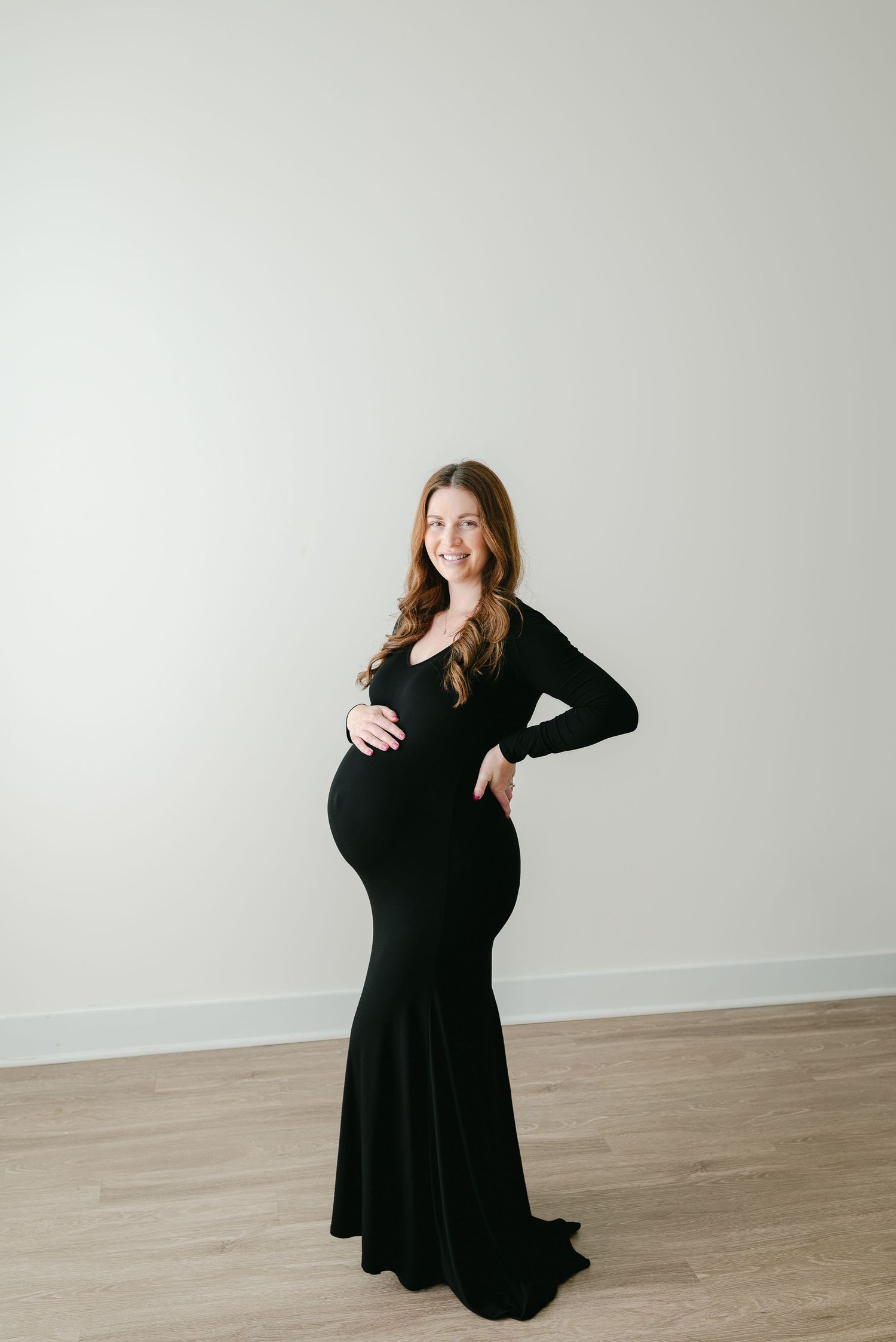 A series of maternity photos showing a woman in a black dress posing against a white wall.
