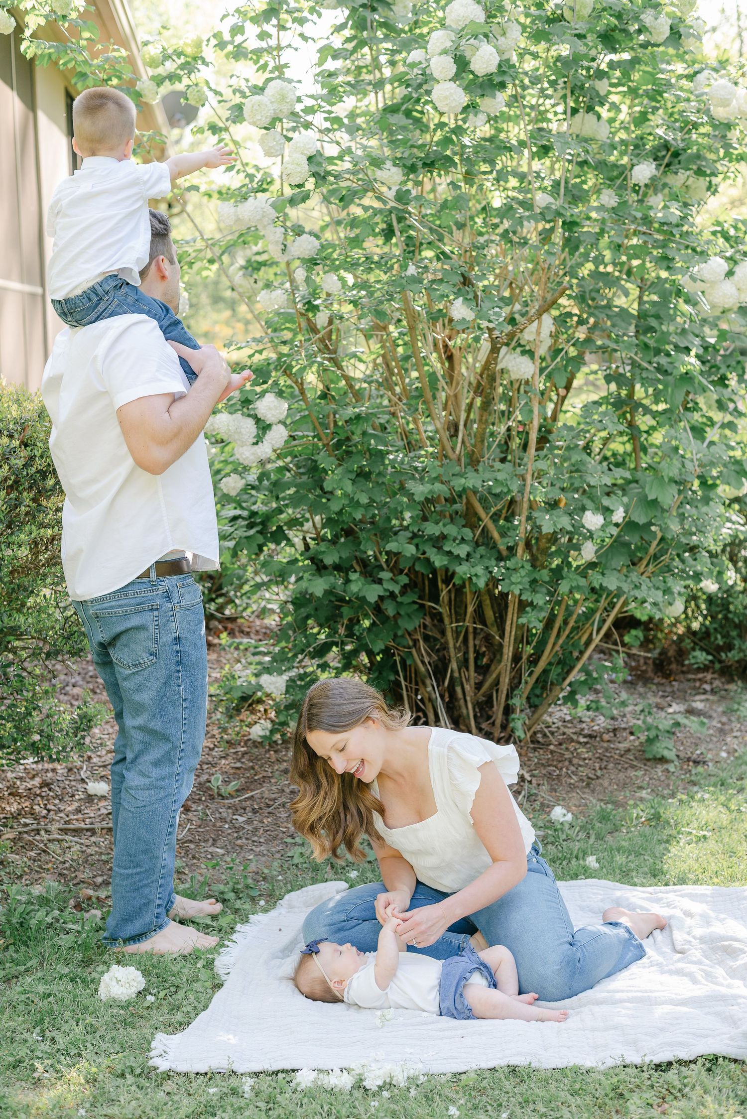Family enjoys tender moments on white blanket in garden setting.