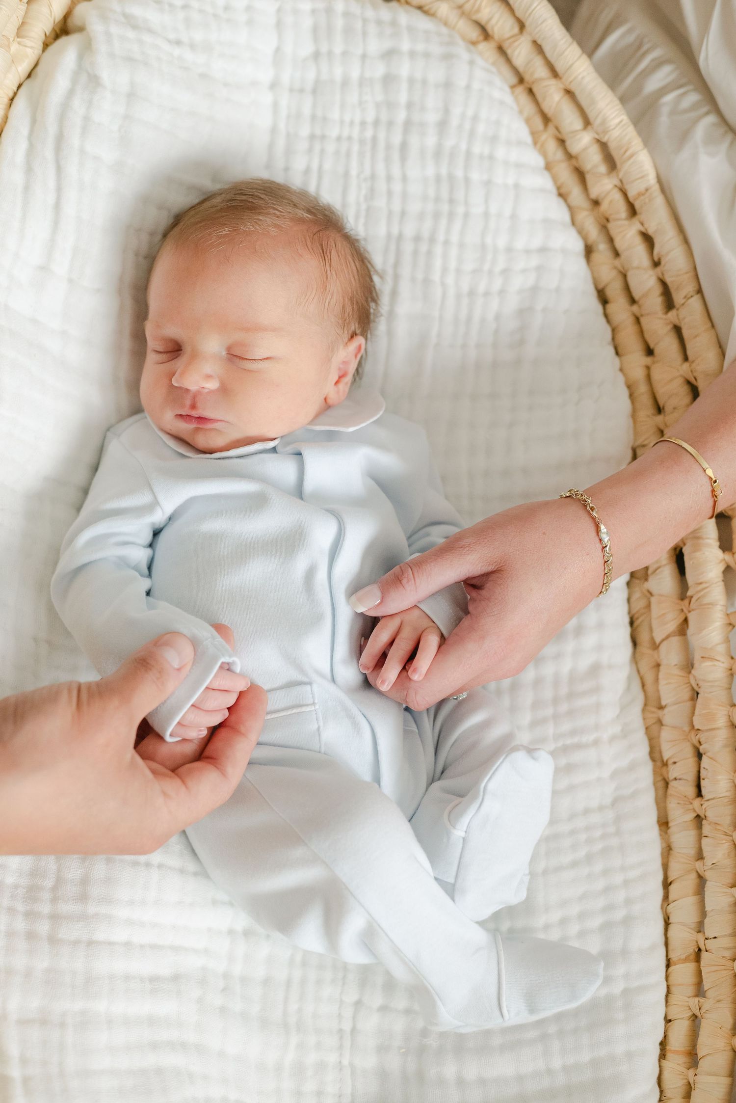 Newborn baby sleeping in woven basket on white textured bedding.