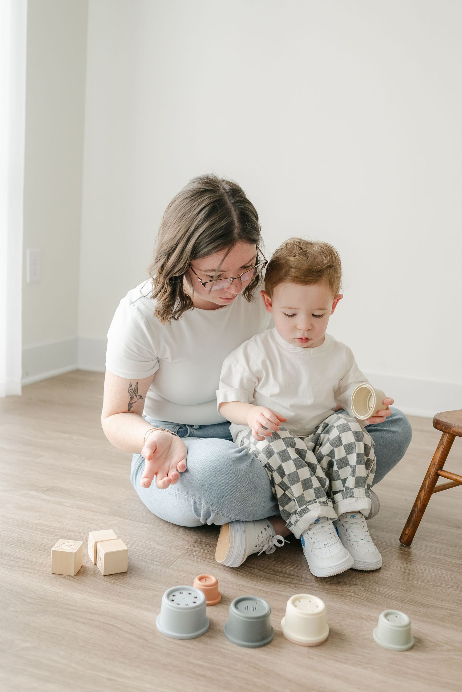 Two people in matching white shirts sit on a wooden floor with small ceramic pots and decorative items.