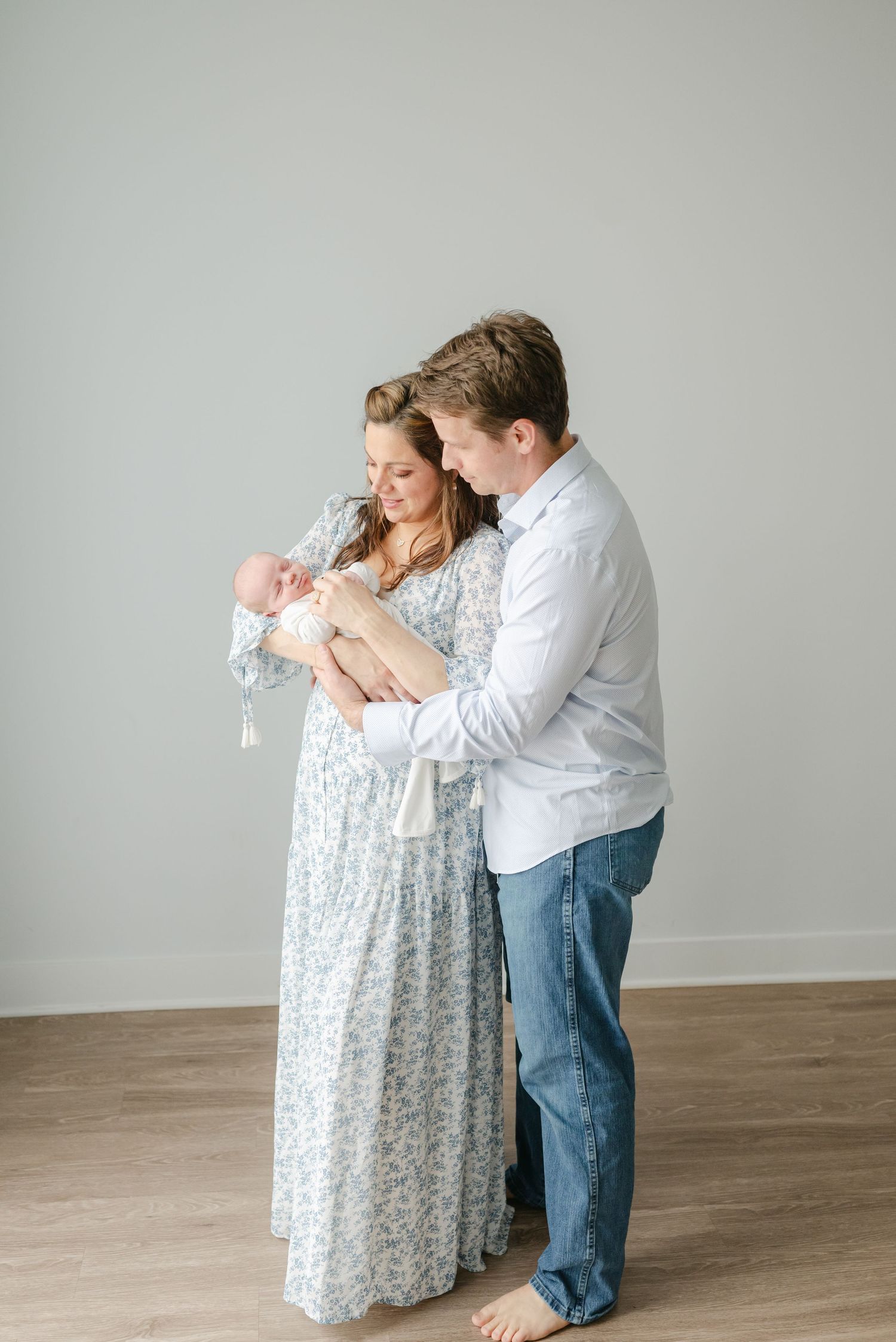 Couple in casual attire lovingly embrace while holding their newborn baby.