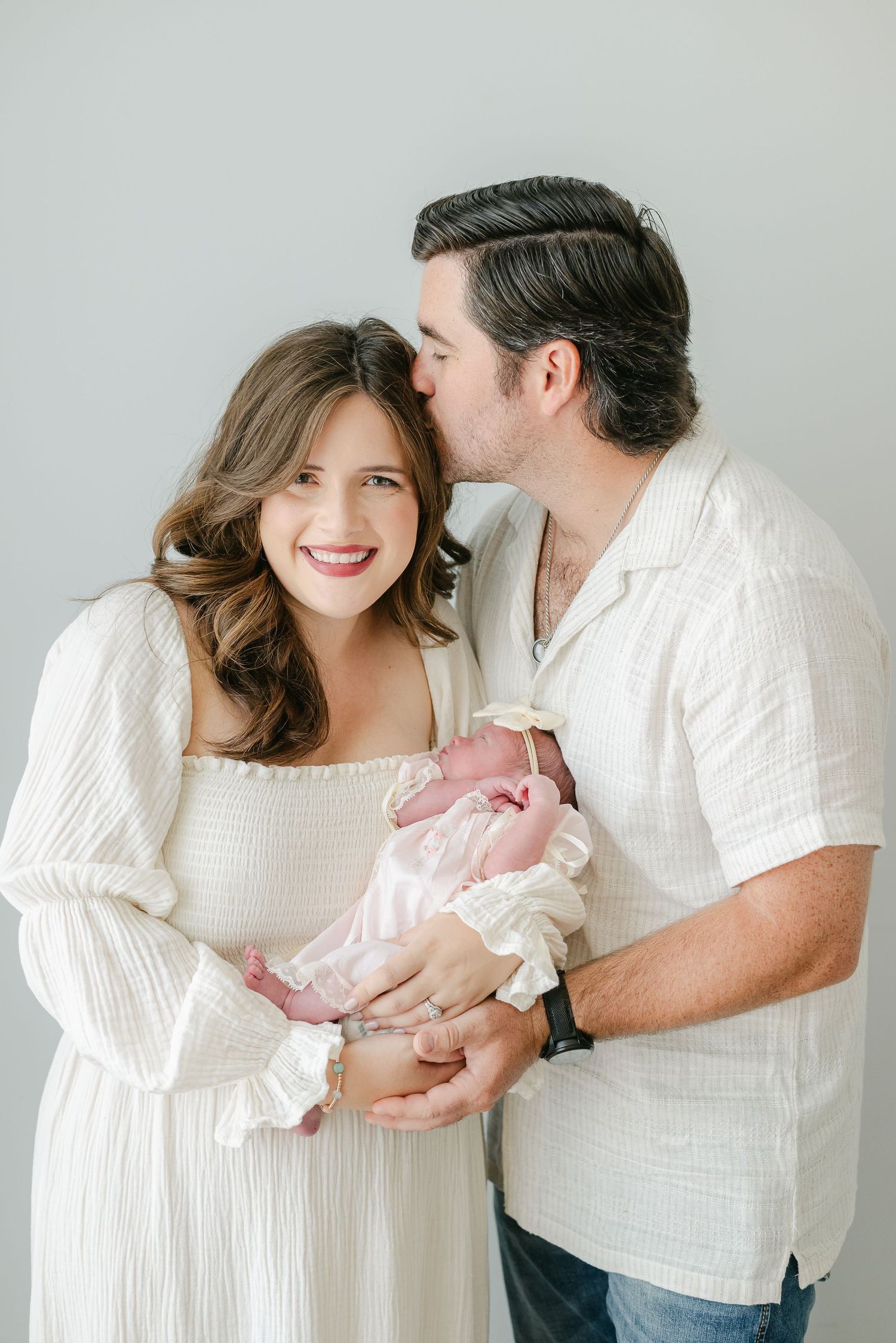 Intimate family moment captured in studio with parents in white holding their newborn.