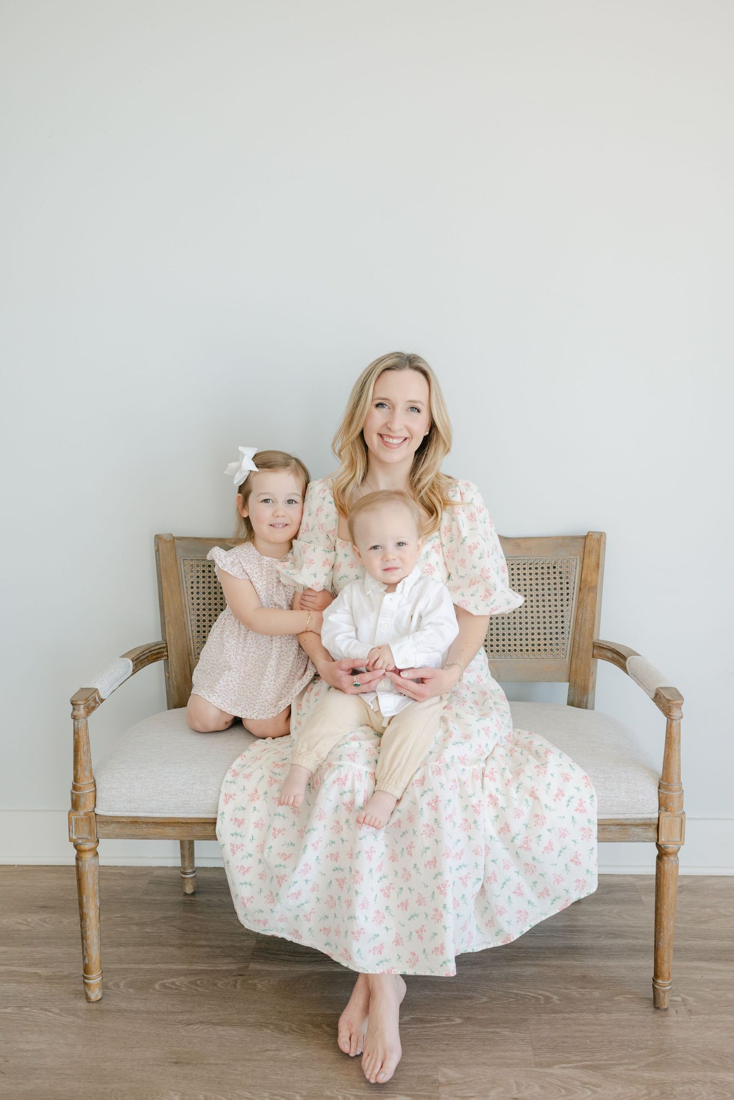 Family photos on a vintage wooden bench showing coordinated white and floral dresses in a bright studio setting.