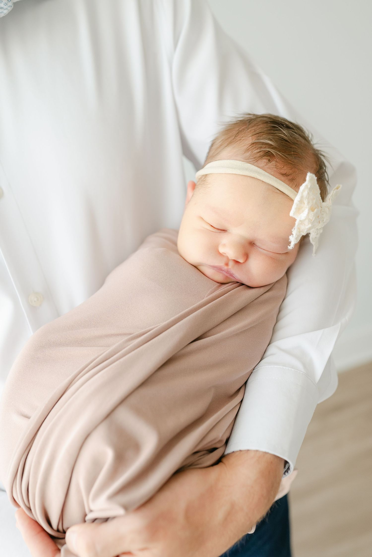 Sleeping newborn wrapped in neutral toned swaddle against minimalist background.