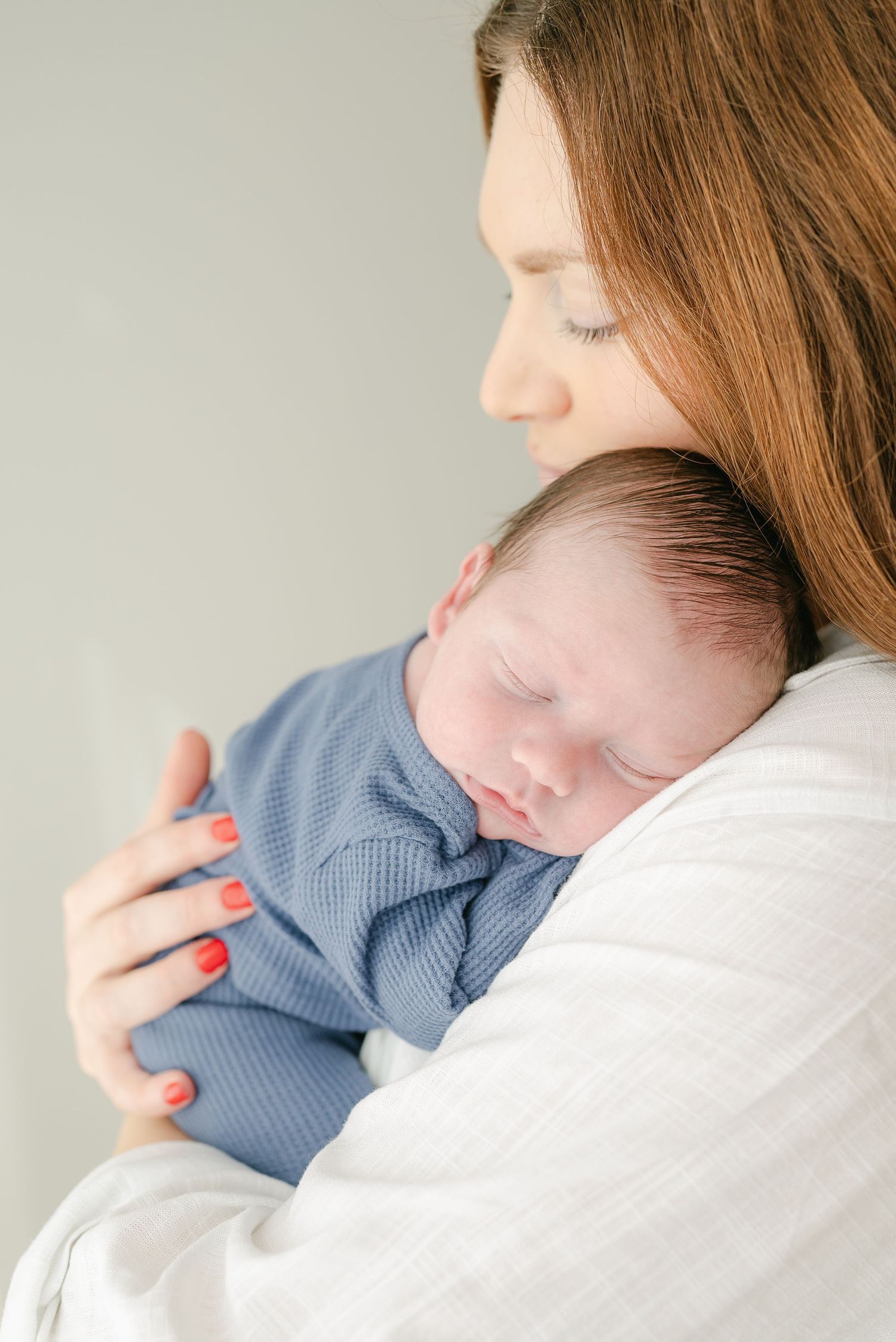 Tender moment of a sleeping baby in a blue sweater being cradled against white fabric.