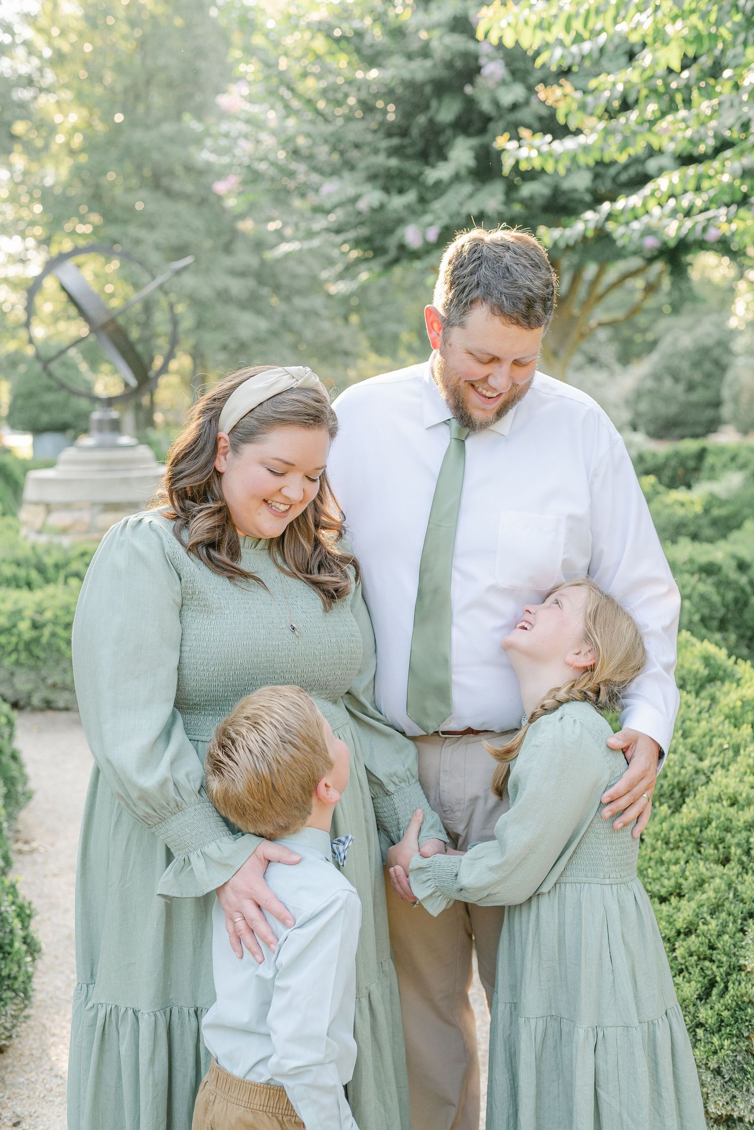 Family of four wearing coordinated sage green outfits sharing a candid moment in a garden.
