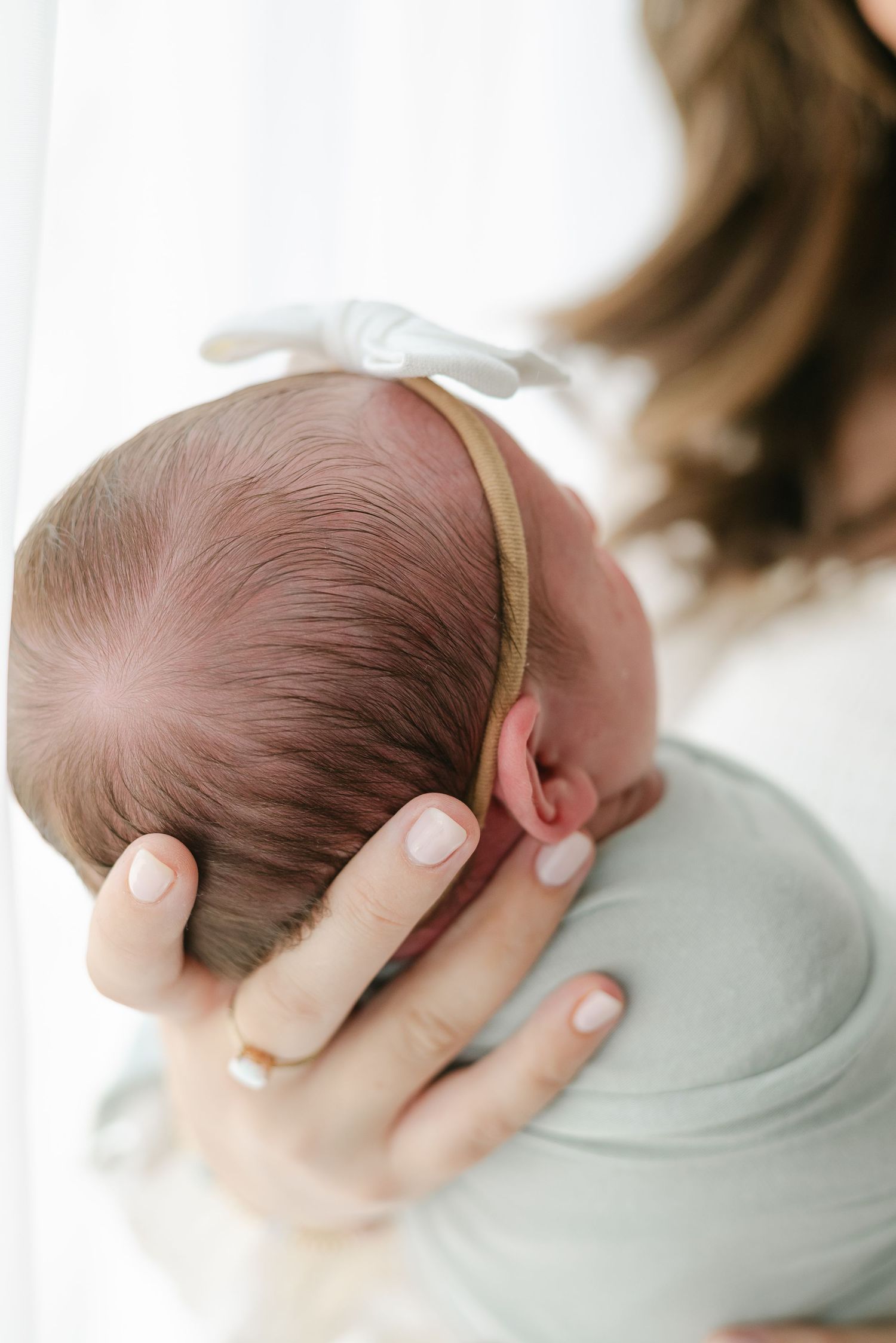 Close-up of hands cradling newborn baby's head against soft white background.