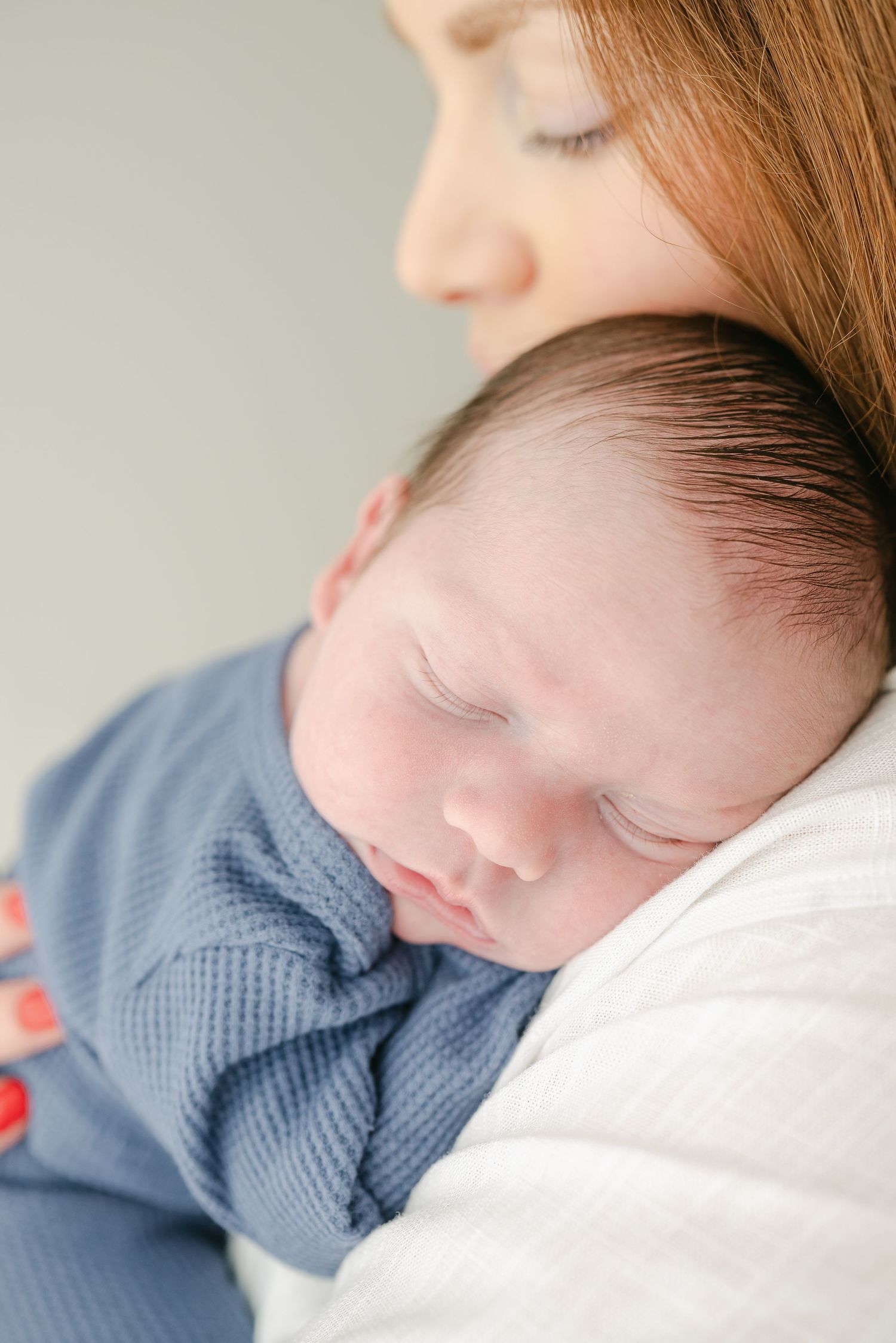 Sleeping baby in blue sweater resting peacefully on mother's shoulder.