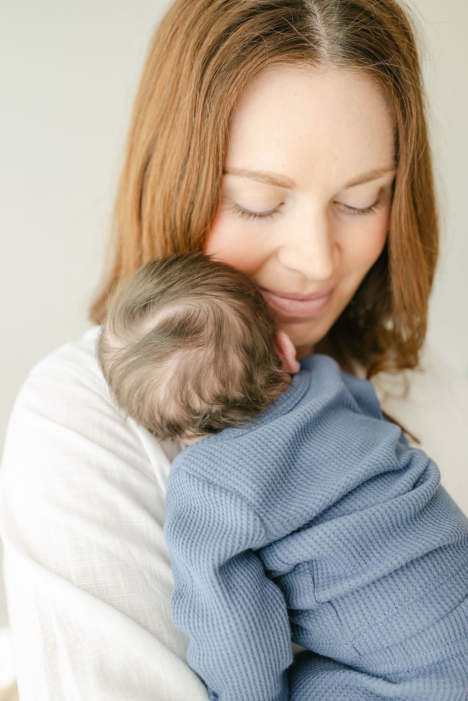 Tender moment between mother and baby in blue sweater against white background.