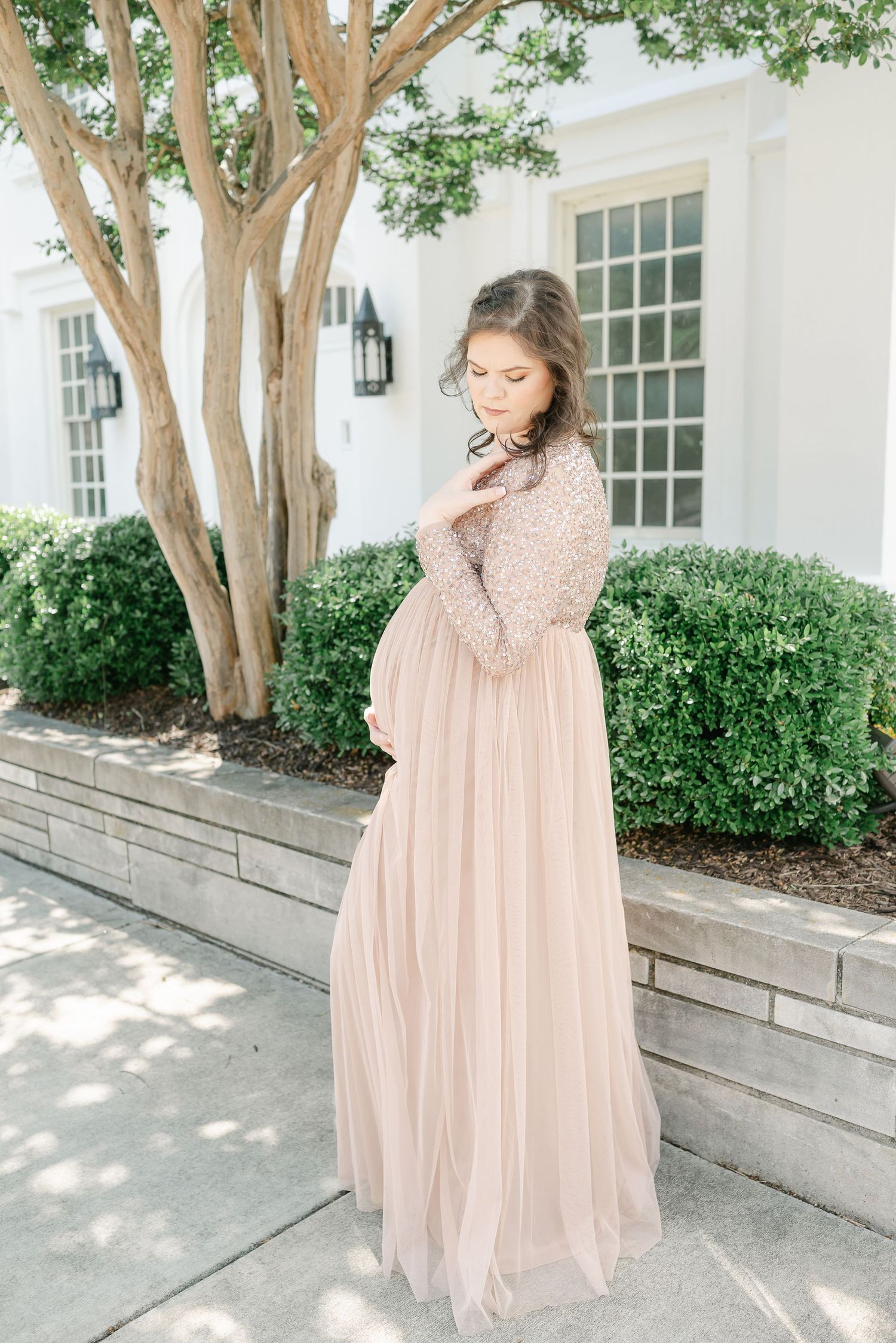 Maternity photoshoot outdoors featuring a blush gown against white colonial architecture.