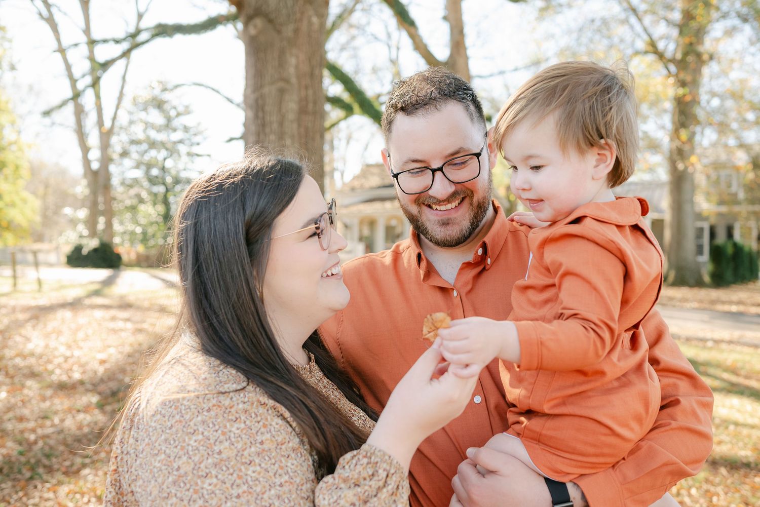 Family wearing coordinating orange outfits posing together outdoors in autumn setting.