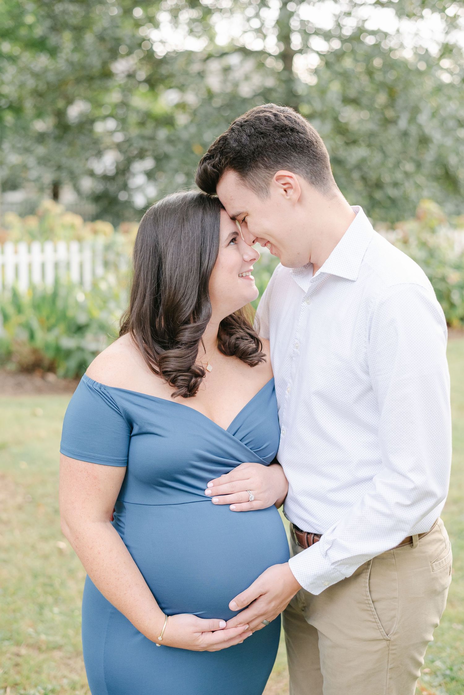 A couple embraces outdoors, with one wearing blue and the other in white.