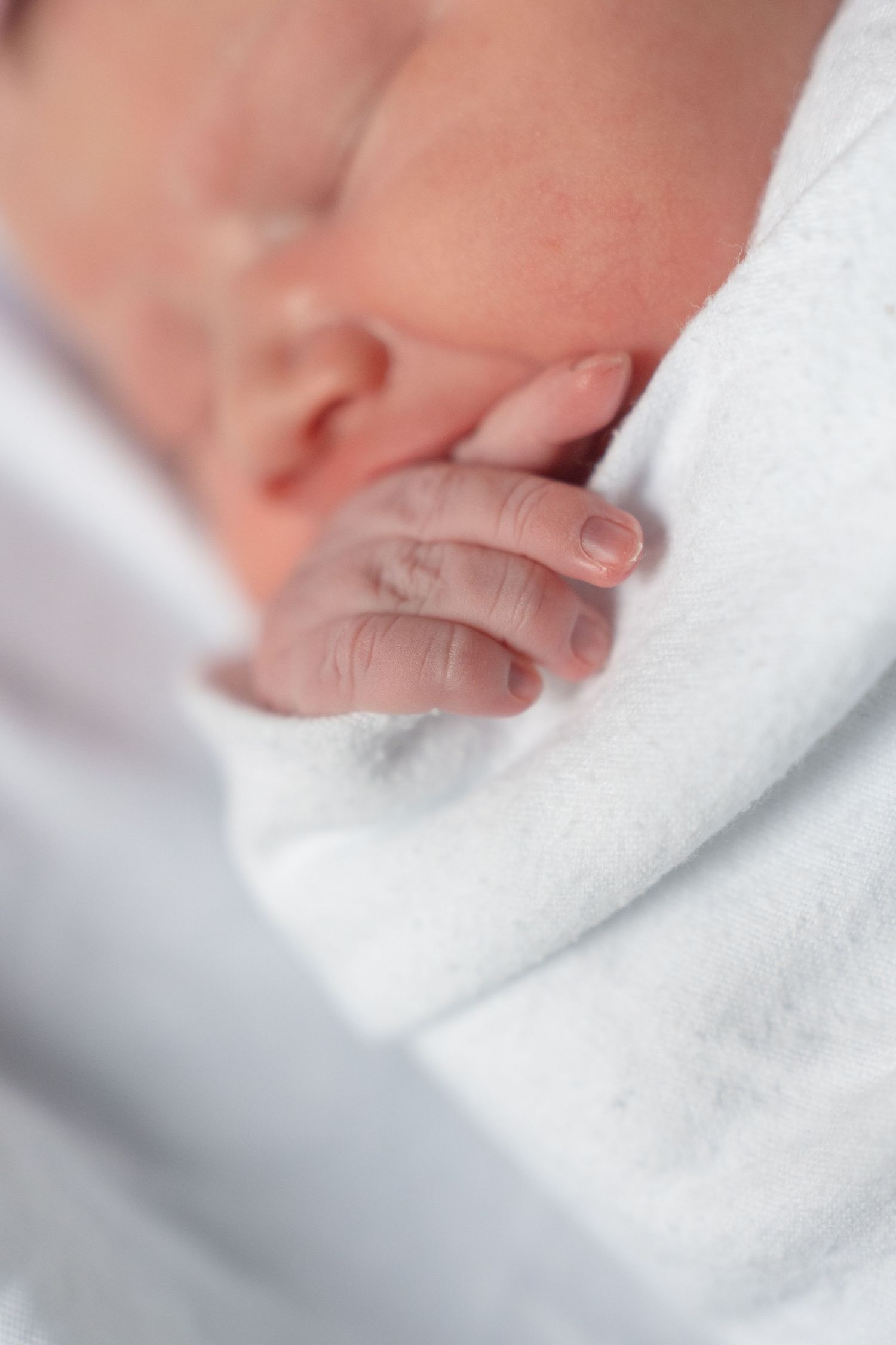 Tiny newborn baby hand resting peacefully on soft white blanket.