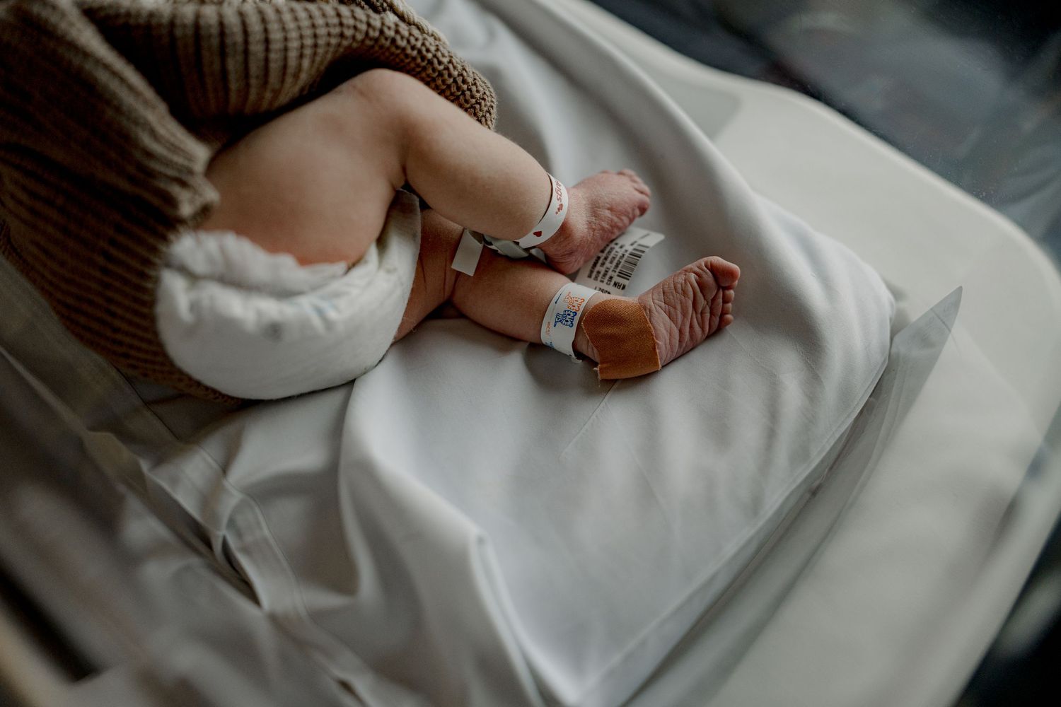Close-up view of a newborn baby's feet wearing knitted brown booties against white blanket background.